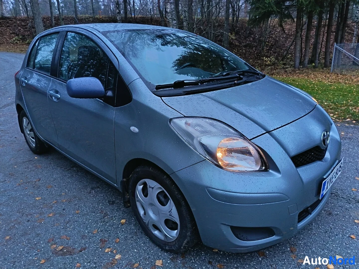 Etuviisto, nokka oikealle: Hopeanharmaa viistoperäinen henkilöauto etukulmasta oikealta, ajoneuvon keula ja etupyörä näkyvät sadesäällä.
