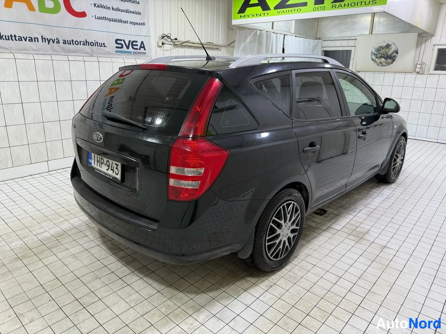 Takaviisto: Kia Ceed -farmari takaa kulmasta, tumma koriväri, takavalojen väliin kuvattu rekisterikilpi ja hienosäädetyt metallivanteet sisätiloissa.