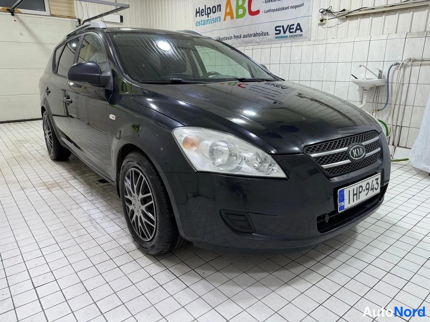 Etuviisto, nokka oikealle: Kia Ceed -farmari edestä kulmasta, tumma koriväri, keulavaloineen ja KIA-merkki konepellin alla, rekisterikilpi etupuskurissa.
