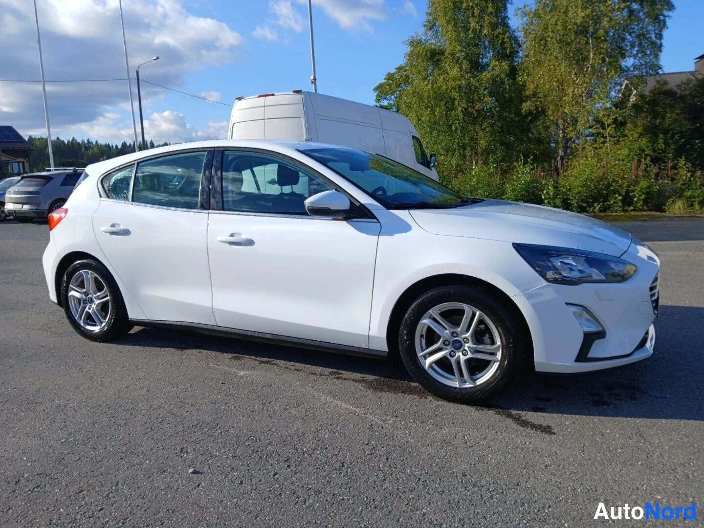 Etuviisto, nokka oikealle: Valkoinen Ford Focus -henkilöauto kolmasosalta edestä oikealle paikoitusalueella; oikea kylki, oikea etuvalo ja ajoneuvon oikea puoli näkyvät.