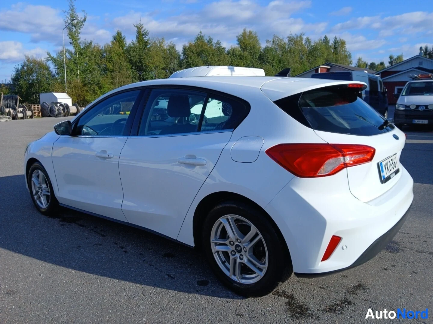 Takaviisto: Valkoinen Ford Focus -henkilöauto kolmasosalta takaa oikealle paikoitusalueella; takavalo, takaluukku ja rekisterikilpi YK0-361 näkyvät.