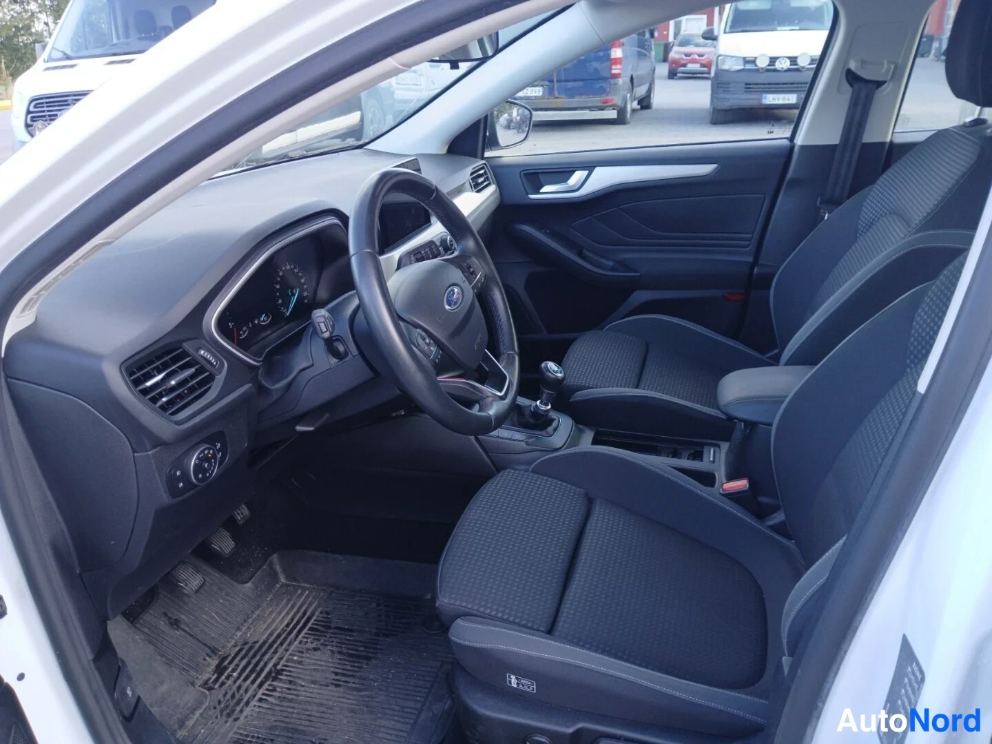 Etuviisto, nokka vasemmalle: Ford Focusin etuistuimet ja kojelauta, manuaalivaihtohecka ja mustat kangasistuimet.