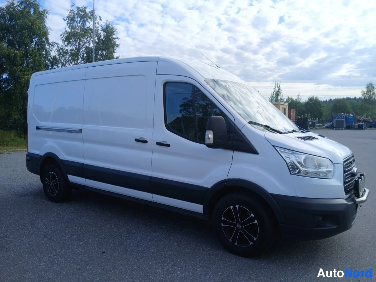 Etuviisto, nokka oikealle: Valkoinen Ford Transit -pakettiauto kolmeneljännesnäkymä edestä, keula oikealla, pitkä korirakenne ja tummat vanteet.