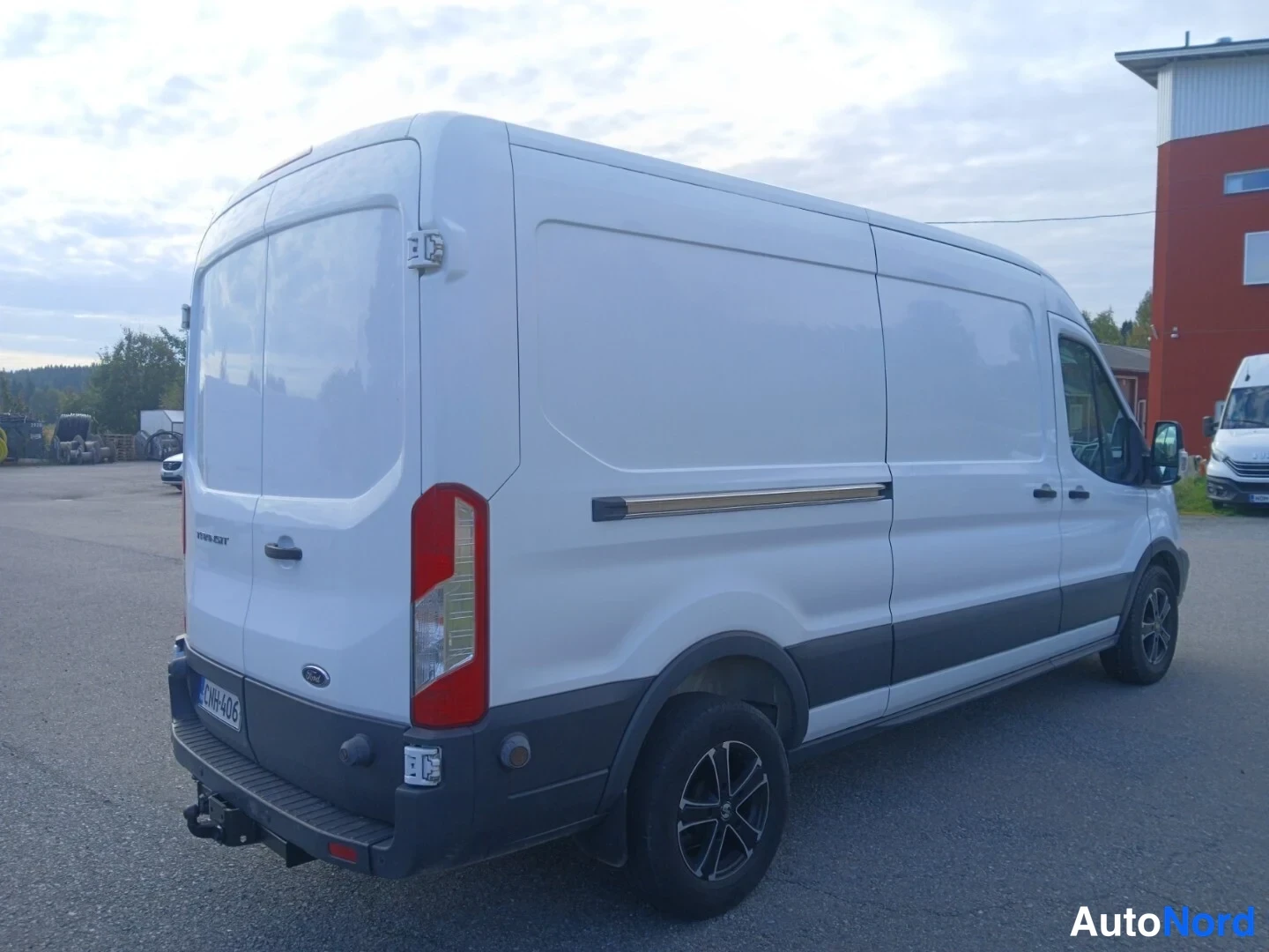 Takaviisto: Valkoinen Ford Transit -pakettiauto takaa kolmeneljännesnäkymästä, takavalot ja peräkoukku näkyvissä, rekisterikilpi.
