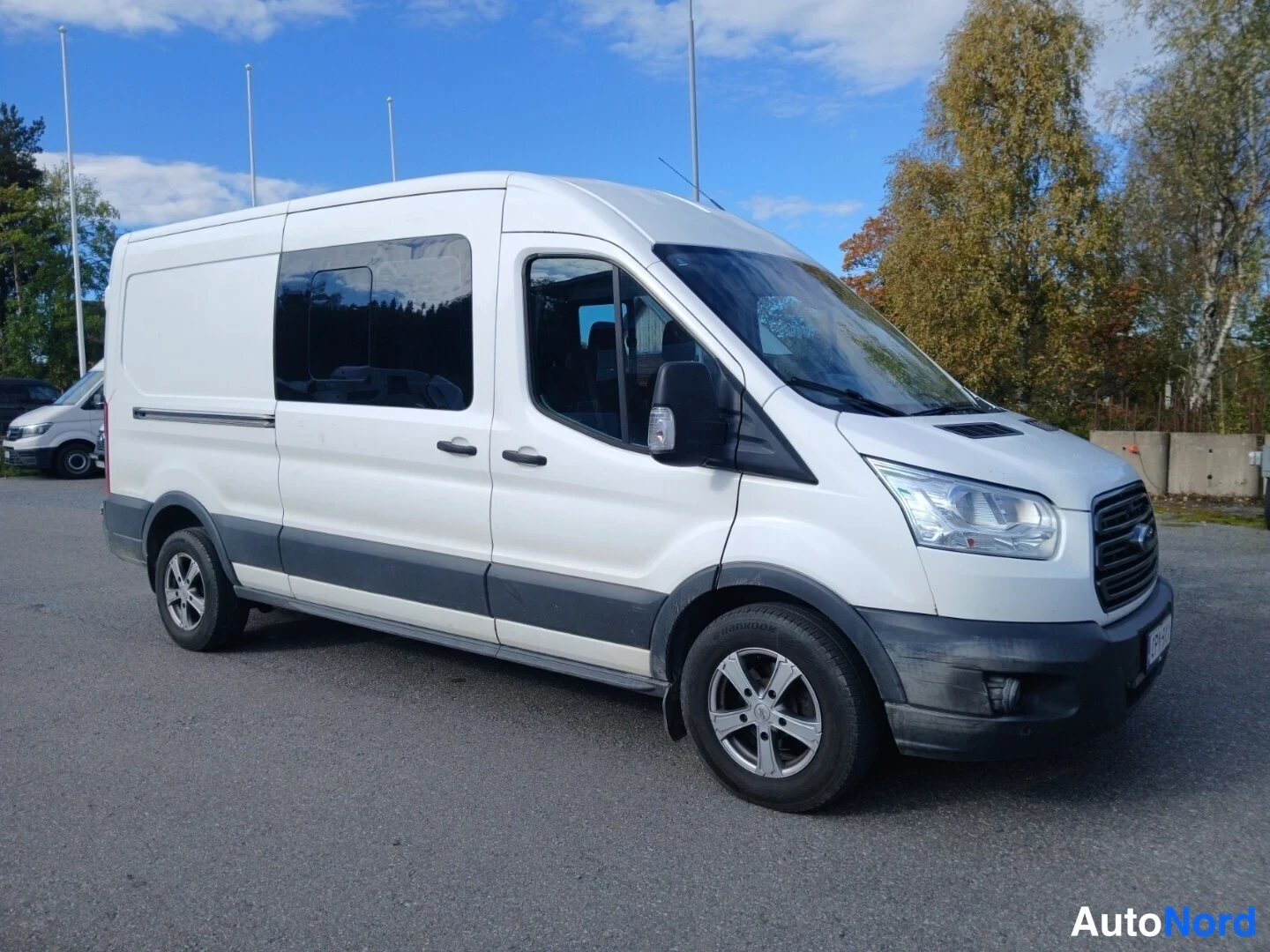 Etuviisto, nokka oikealle: Valkoinen pakettiauto kolmannelta etuviistolta oikealla; etusäleikkö, ajovalot ja auton kylki näkyvissä.