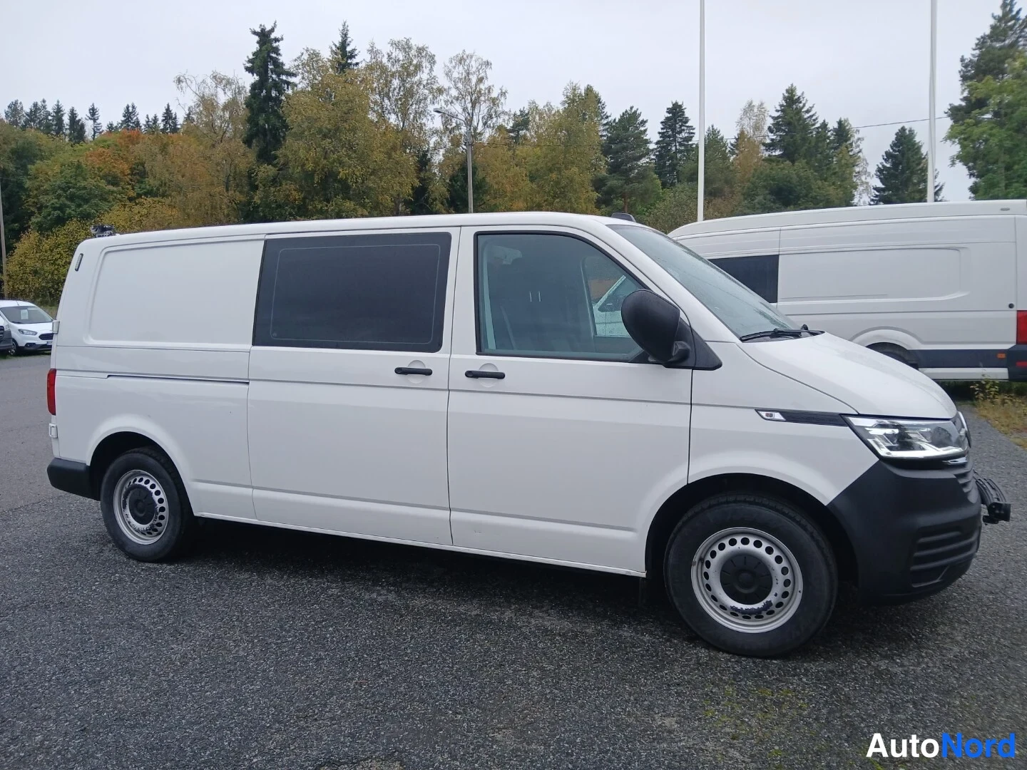 Etuviisto, nokka oikealle: Valkoinen pakettiauto sivulta etviistosta, keula oikealla, tummat takaikkunat.