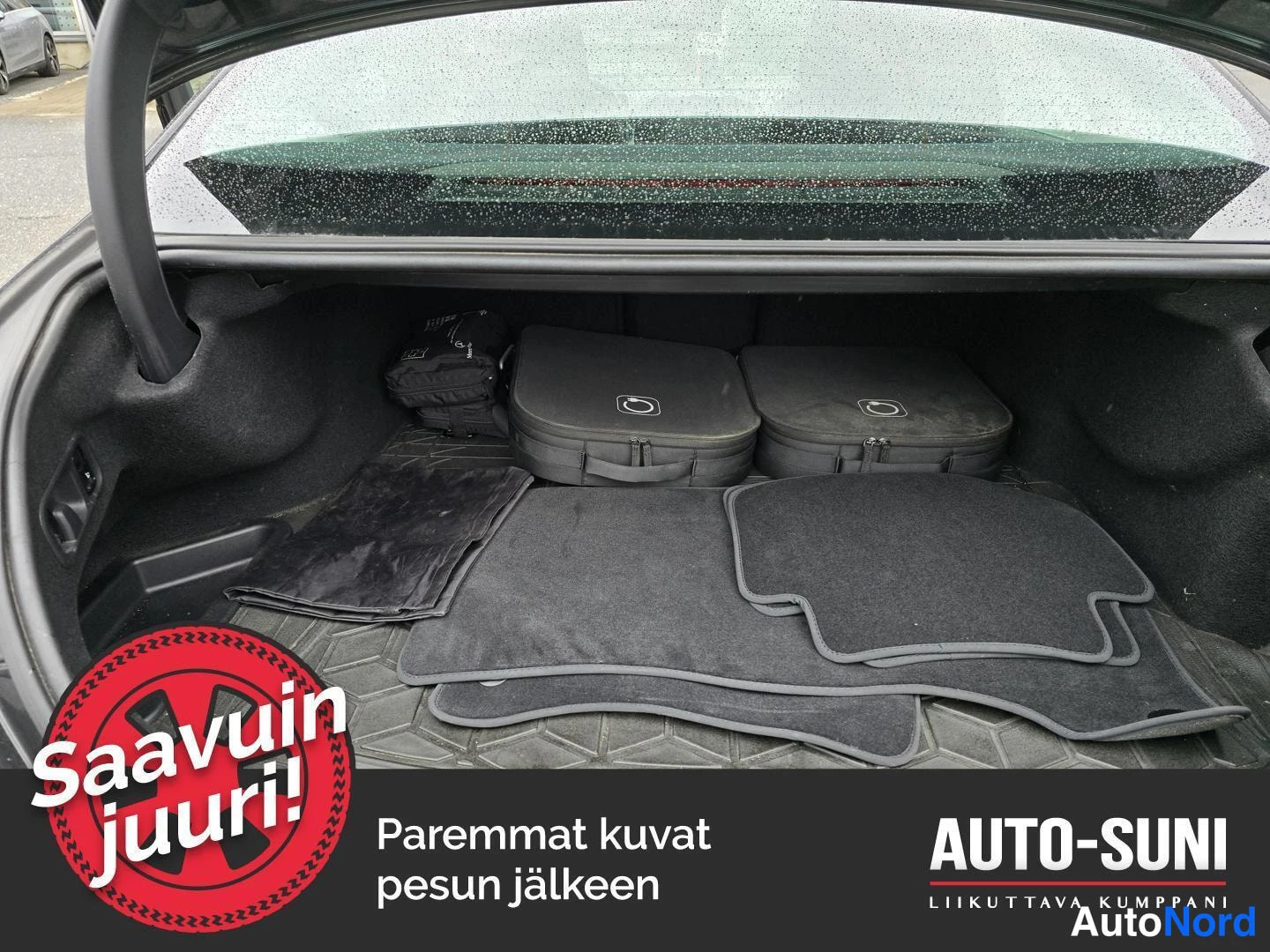 Muu: Auki avattu tavaratila, jossa mustat lattiamatot, kaapelilaukku ja korjaussarjan säilytyspussit.