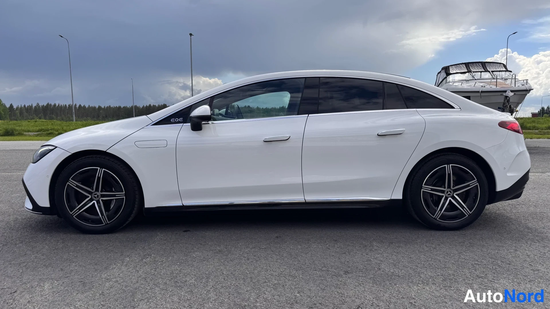 Sivulta: Valkoinen Mercedes-Benz EQE -sedan sivukuva vasemmalta,Mustat ikkunoiden karjat ja kromilistat ovissa, mustat kevytmetallivanteet.