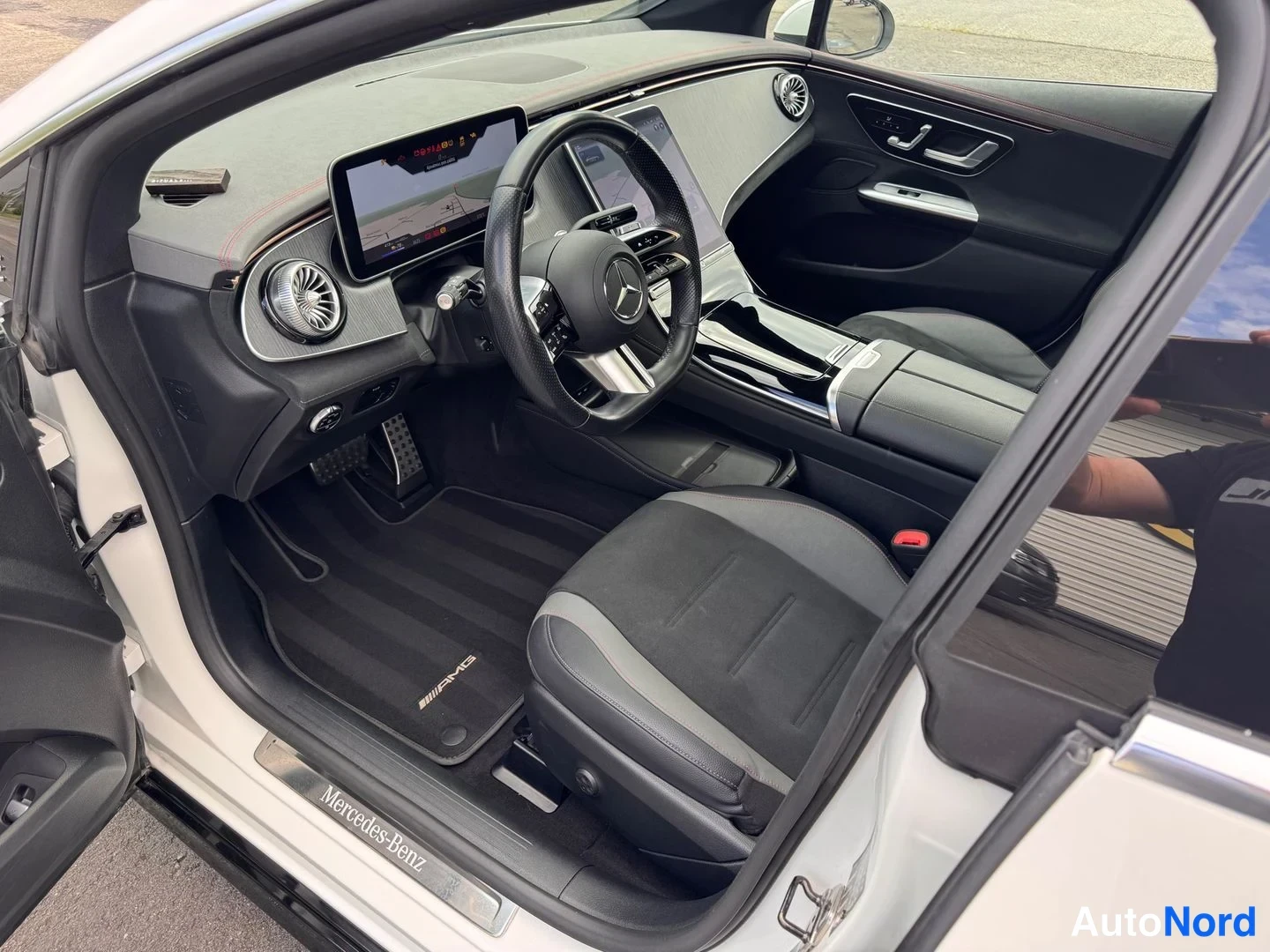Muu: Avoimen kuljettajan oven sisäännäkyvä Mercedes-Benzin ohjaamo: tumma kojelauta ja mm. AMG-merkillä varustettu matto.