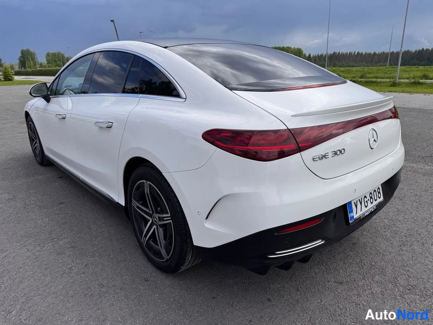 Takaviisto: Valkoinen Mercedes-Benz EQE 300 sedan takakulma oikealta,Punaiset poikittain asennetut takavalot, musta basattikolmiot, rekisterikilpi.