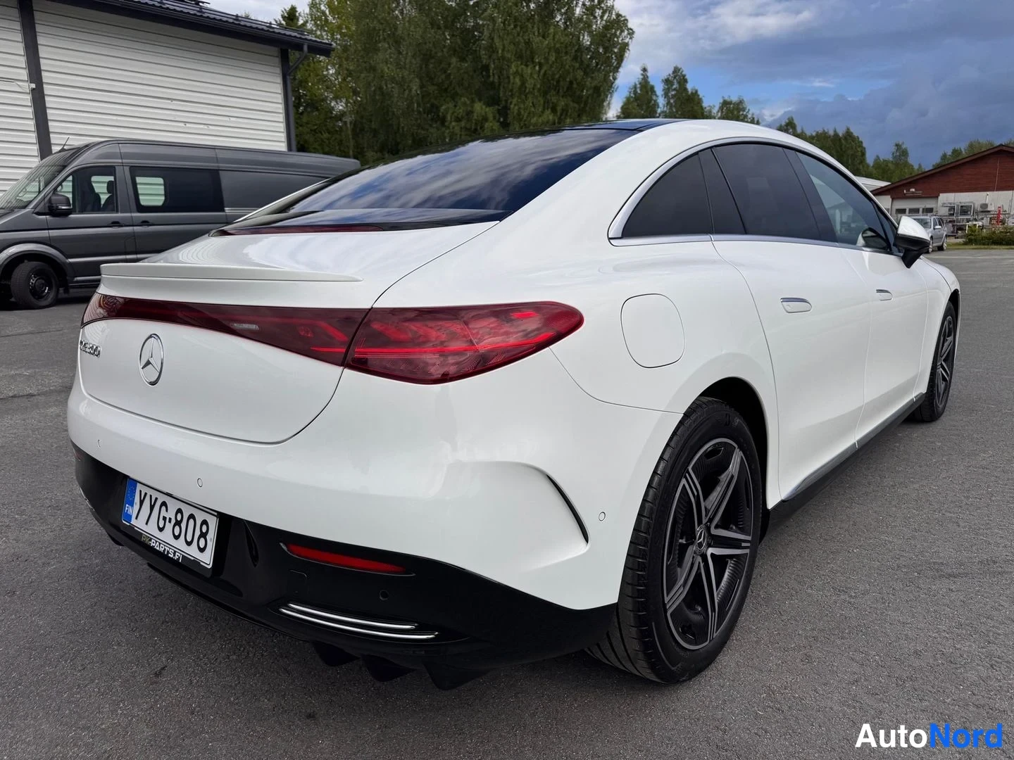 Takaviisto: Valkoisen sedanin takaosa ja oikea kylki kolmesta neljäsosaan takaa kuvattuna; punaiset takavalot, Mercedes-tähti kannessa ja rekisteritunnus.