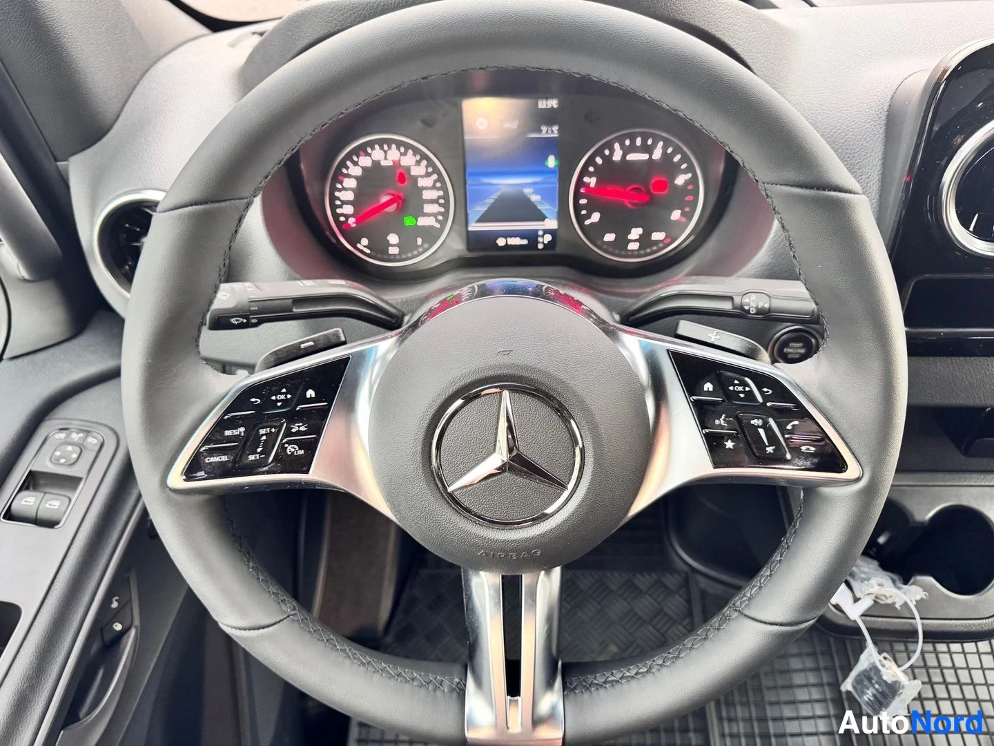 Muu: Lähikuva Mercedes-ohjauspyörästä, jossa AIRBAG-merkki ja napin klusterit; taustalla analoginen mittaristo ja keskinäyttö.