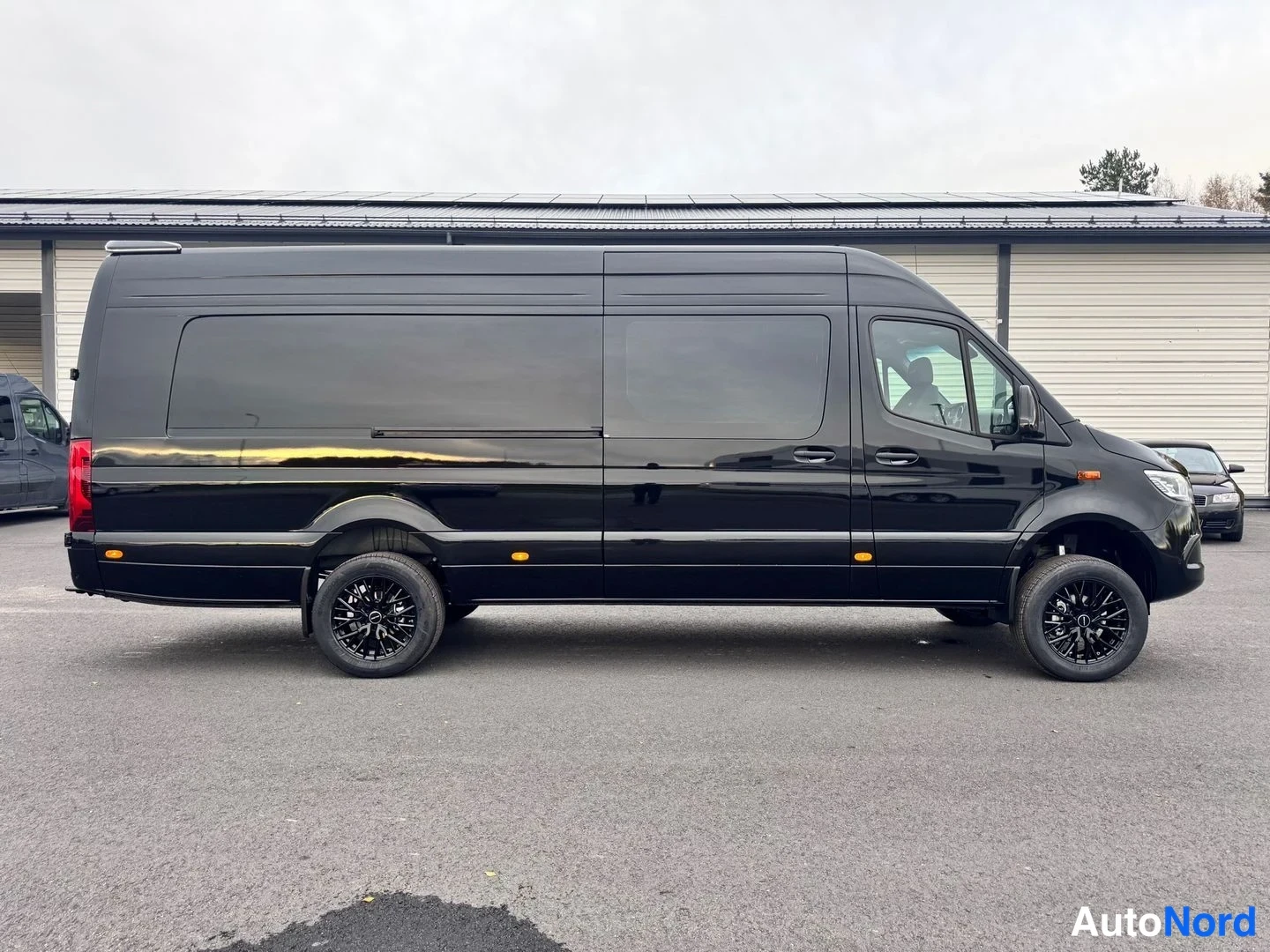 Etuviisto, nokka oikealle: Musta Mercedes-Benz Sprinter -pakettiauto sivukuvassa, tummat kevytmetallivanteet ja takavalo näkyvissä.