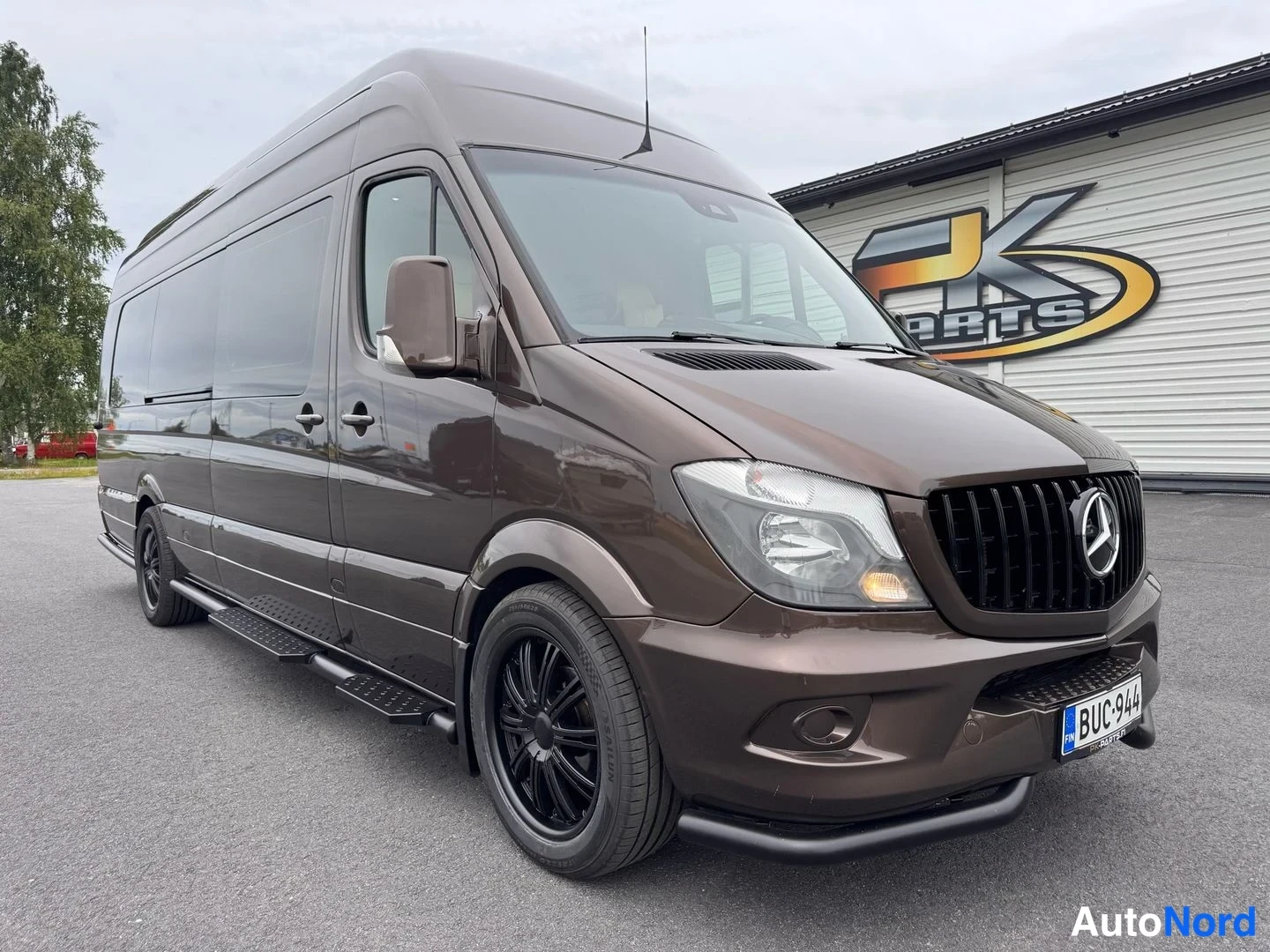 Etuviisto, nokka oikealle: Ruskea Mercedes-Benz Sprinter -pakettiauto kolmesta neljänneskulmasta edestä oikealta, mustat kevytmetallivanteet ja rekisterikilpi.