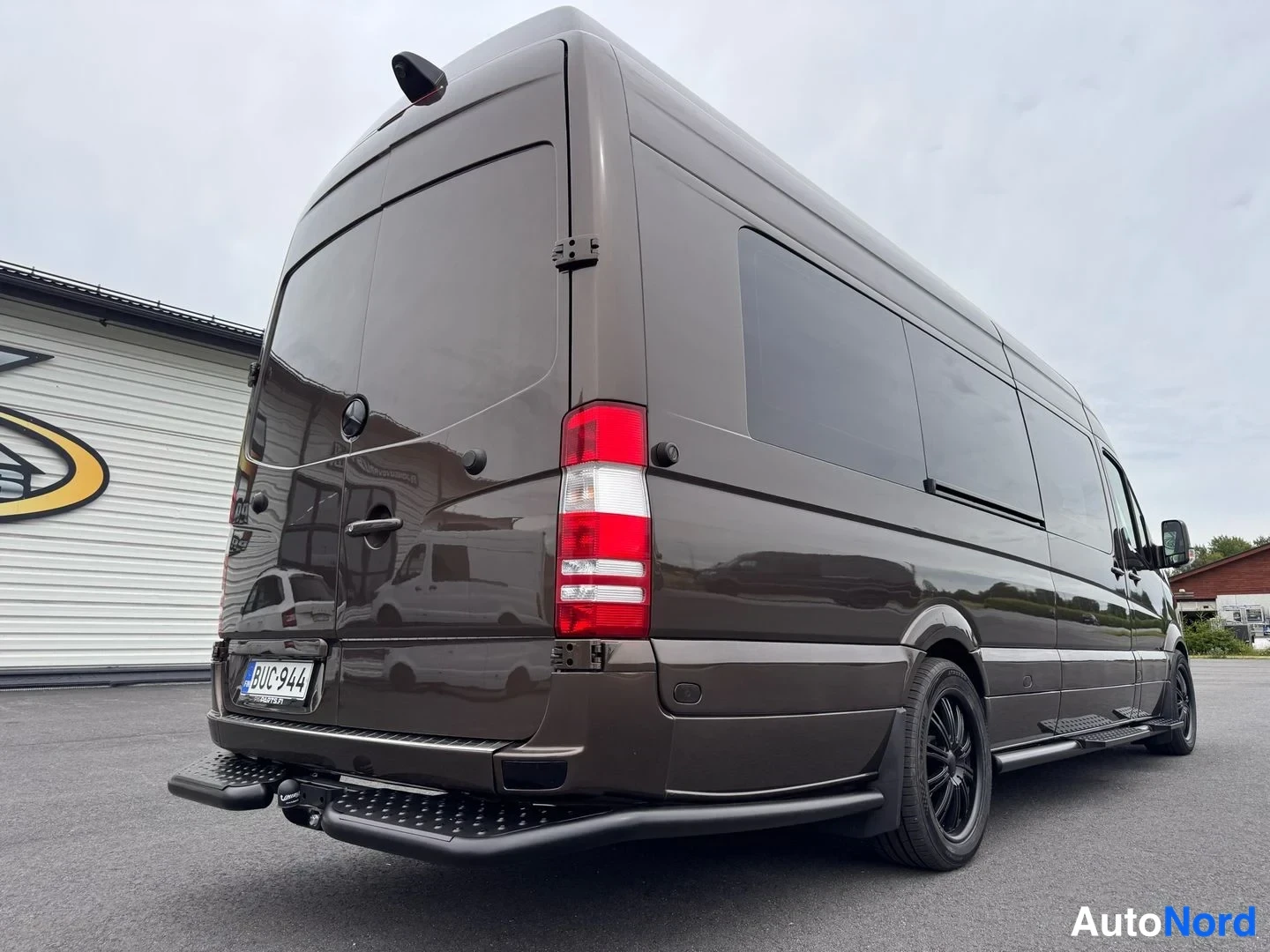 Takaviisto: Ruskea Mercedes-Benz Sprinter -pakettiauto takaa vasemmalta kolmesta neljänneskulmasta, punaiset takavalot ja rekisterikilpi.