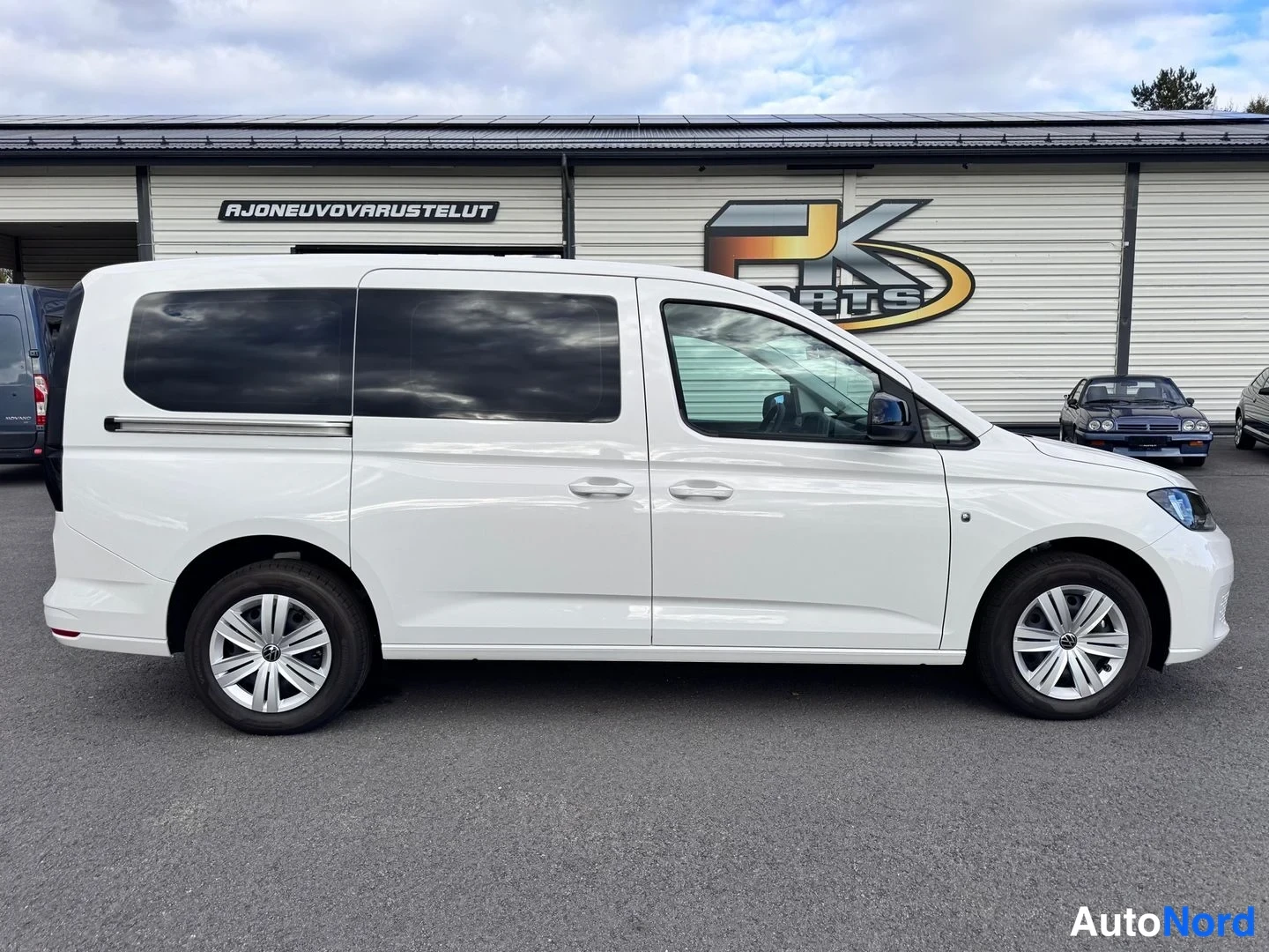 Sivulta: Valkoisen Volkswagen Caddy -pakettiauton vasen kylki sivulta kuvattuna autotallin edessä.