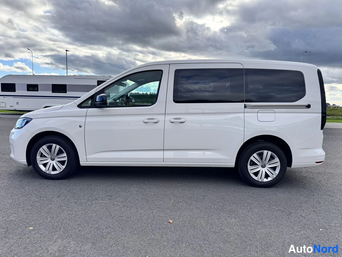 Sivulta: Volkswagen Caddy Maxi -pakettiauto sivulta, valkoinen korimalli vasemmasta sivusta kuvattuna avoimella paikalla.