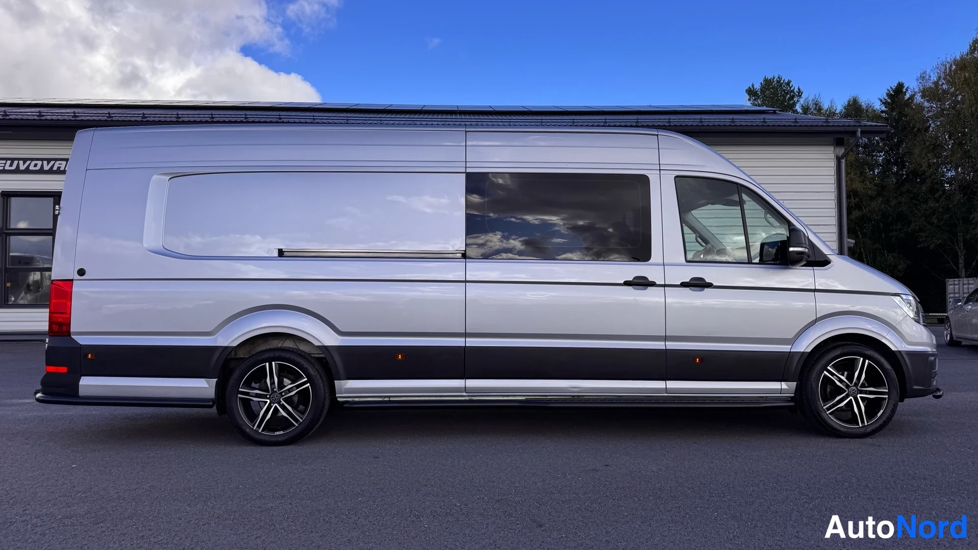 Sivulta: Volkswagen Crafter -pakettiauto sivulta, tummat ikkunat ja mustat pyörät.