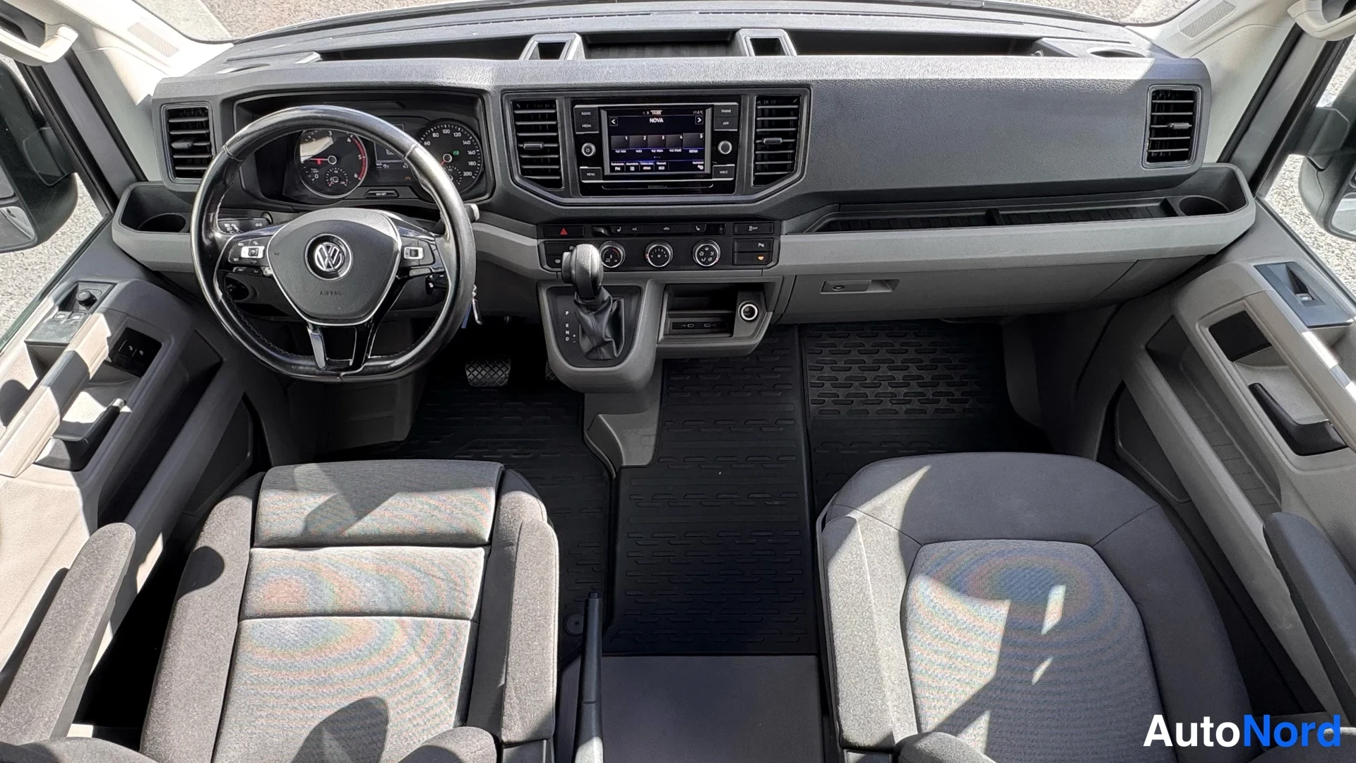 Edestä: Ohjaamo edestäpäin: Volkkarin ohjauspyörä, mittaristo, kosketusnäytöllinen radio, automaattivaihteen valitsin ja kaksi etuistuinta.