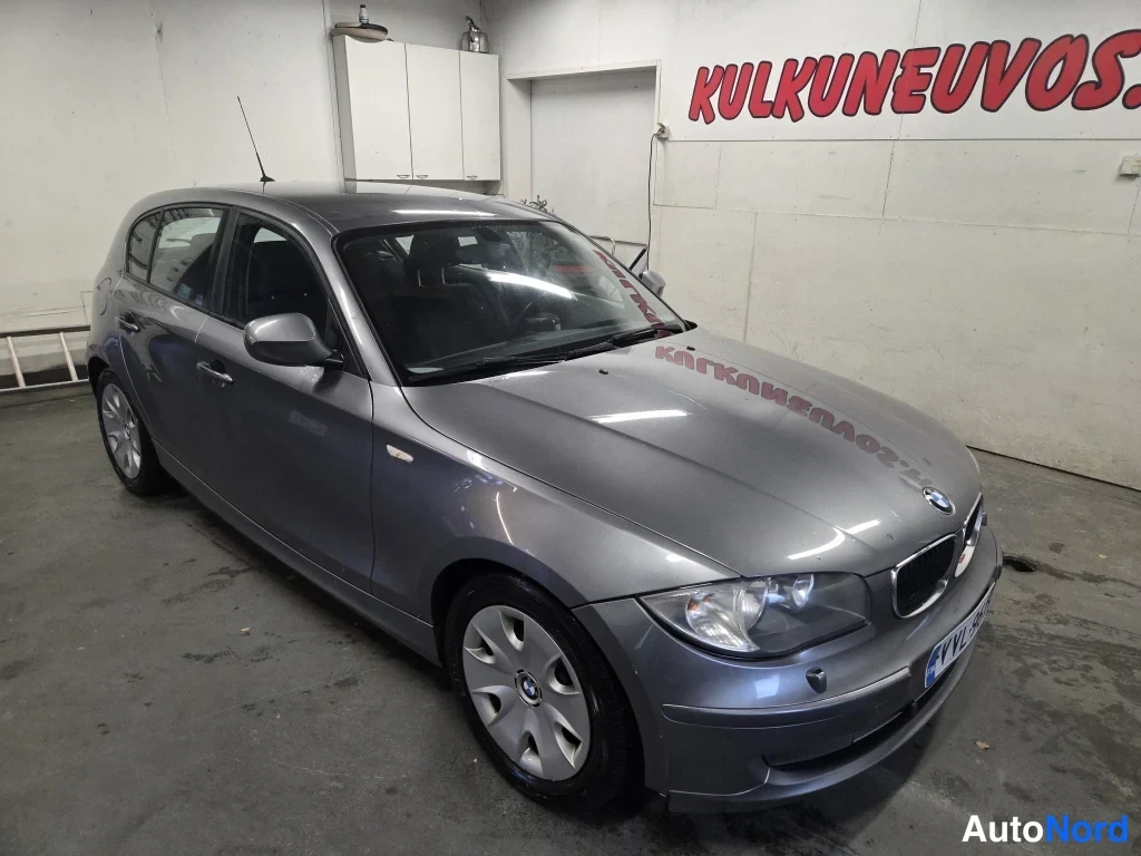 Etuviisto, nokka oikealle: BMW 1-sarjan viistosti kuvattu etunäkymästä, harmaa viistoperä pysähdyksissä hallissa.