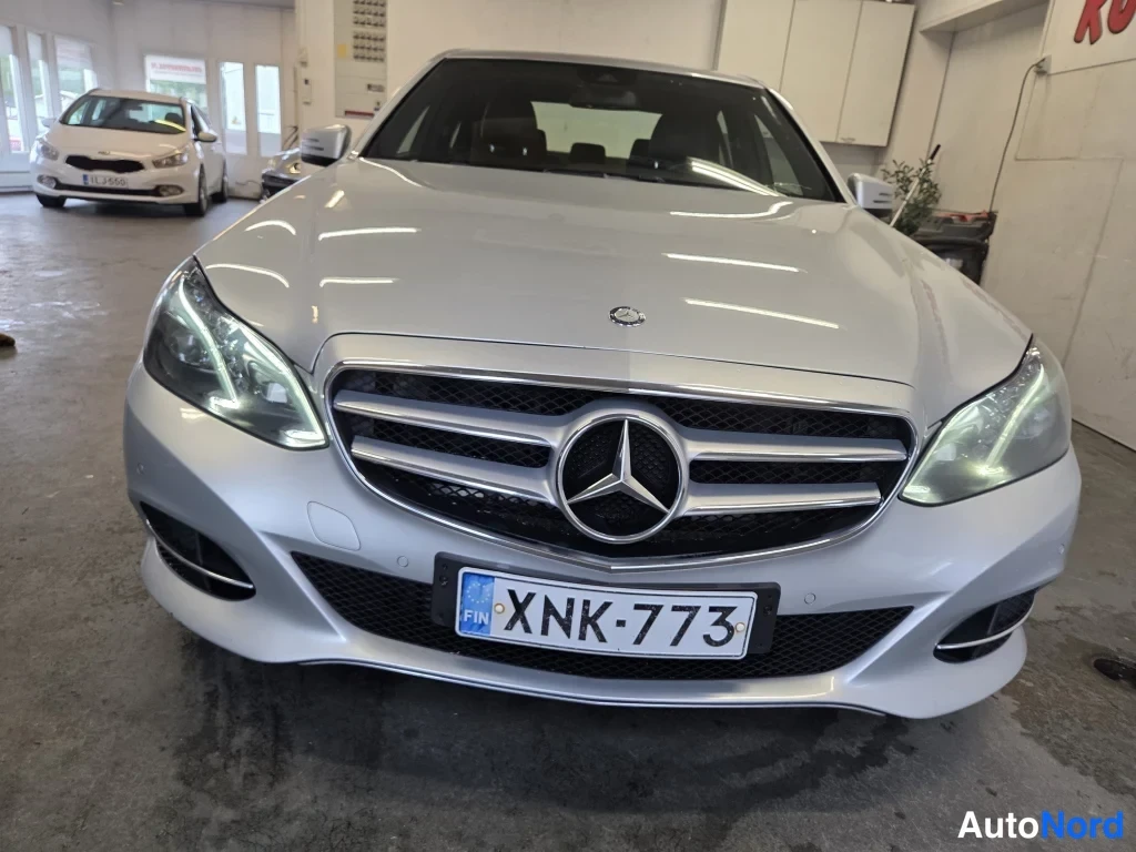 Edestä: Mercedes-Benzin etunäkymä hallissa: tähtimerkki etusäleikössä, LED-päiväajovalot ja rekisteri.