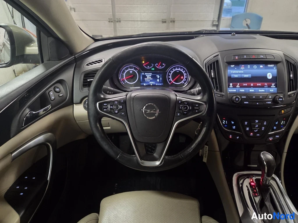 Muu: Ohjaamon näkymä Opel-ohjauspyörän takaa: mittaristo, kosketusnäyttöradio ja automaattivaihteiston valitsin.