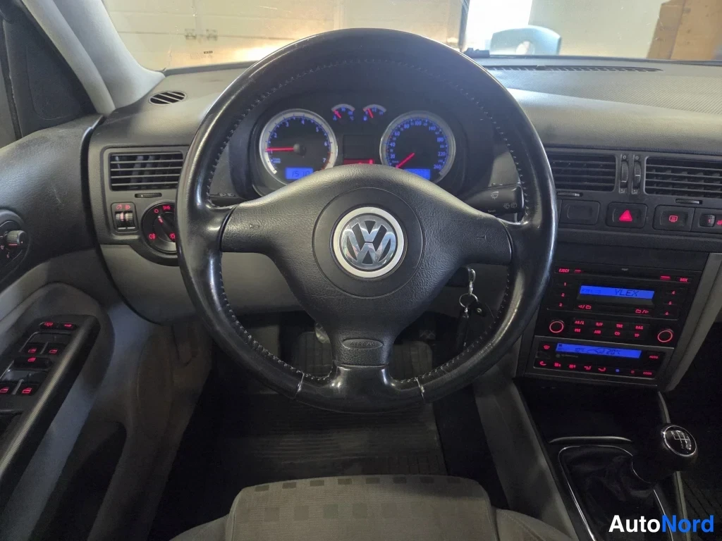 Muu: Ohjauspyörä ja mittaristo lähikuvassa, Volkswagenin merkki näkyy ohjauspyörän keskellä, radio ja manuaalivaihteiston vaihdekeila osittain näkyvissä.