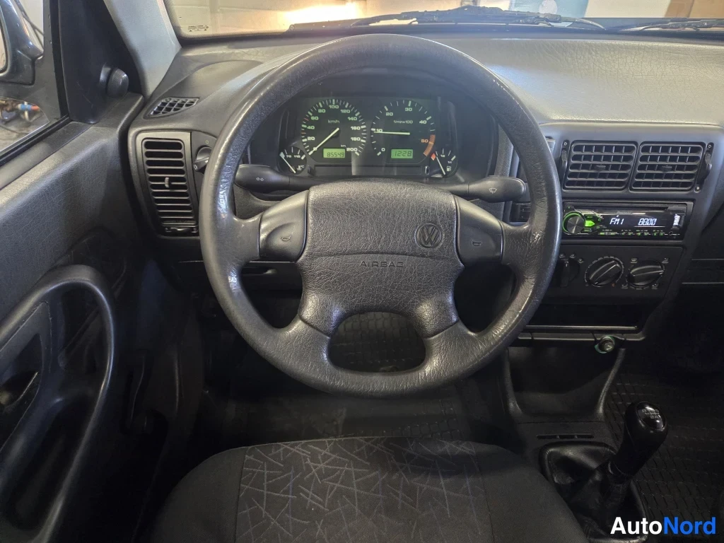 Muu: Ohjauspyörän ja kojelaudan näkymä: VOLKSWAGEN AIRBAG -merkkien sisältävä ohjauspyörä, mittaristo ja radioyksikkö.
