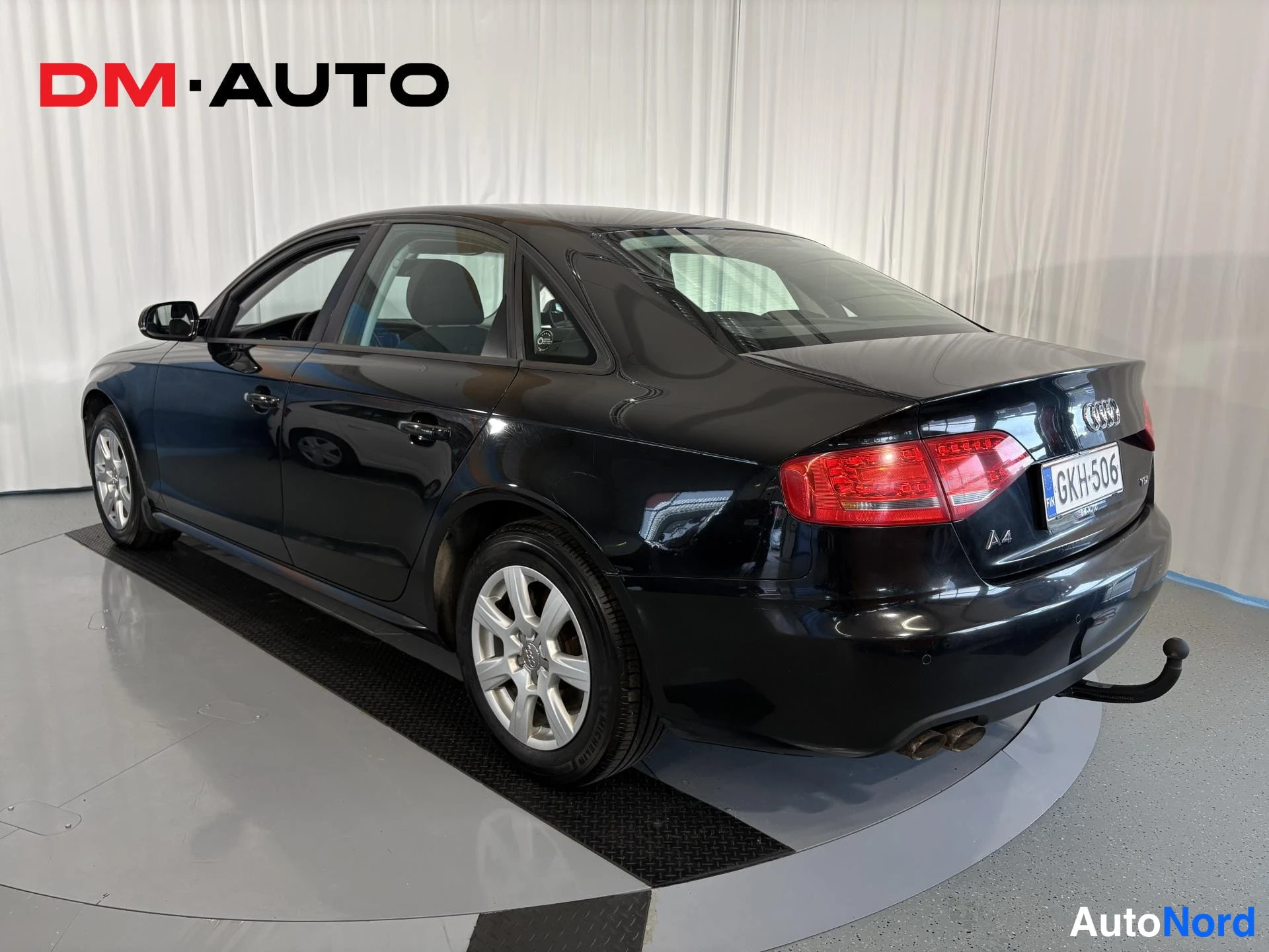 Takaviisto: Audi A4 -sedan takaosa ja oikea sivu kolmannesnäkymässä; musta koripinta, takavalo, rekisterikilpi, A4-merkintä, kaksi pakoputkea ja perävaunukoukku.