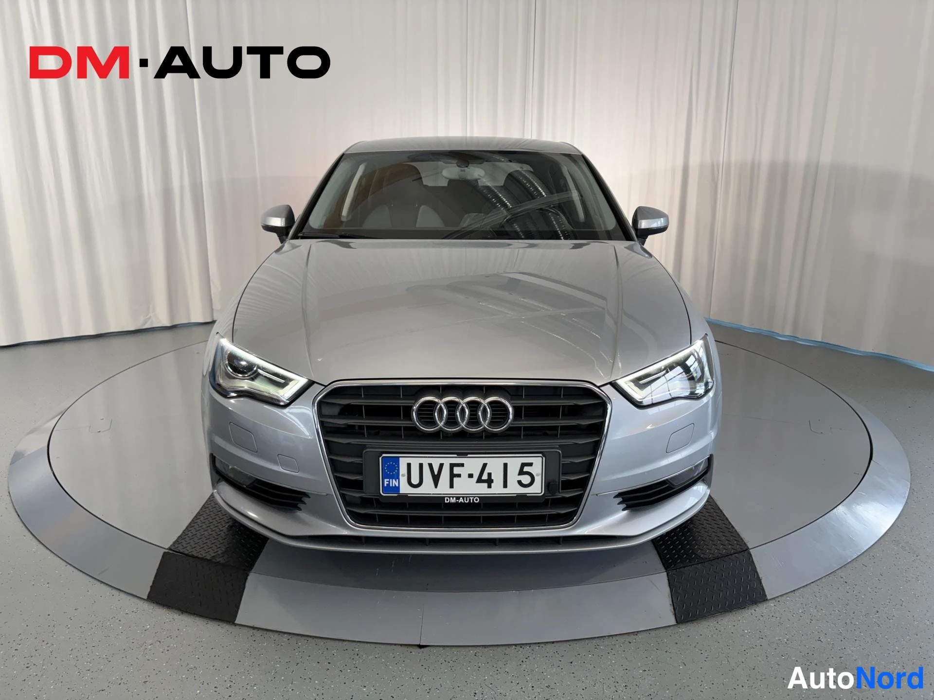 Edestä: Hopeanharmaa Audi A3 -sedan suoraan edestä; etusäleikössä Audi-merkki, rekisterikilpi ja LED-ajovalot.