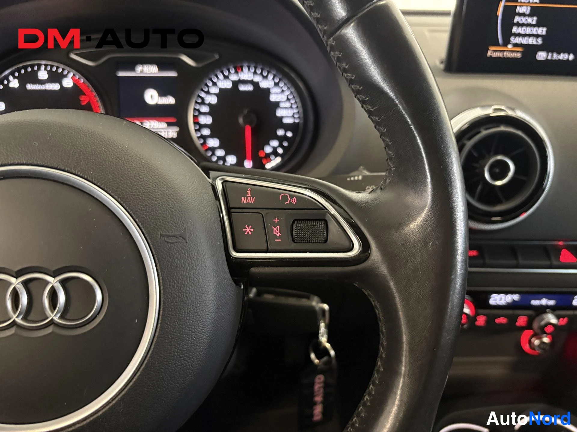 Edestä: Ohjauspyörä ja mittaristo lähikuvassa: Audi-merkki,Multiinfo-näyttö ja infotainment-näyttö oikealla, vaihteen hello P-asennossa.