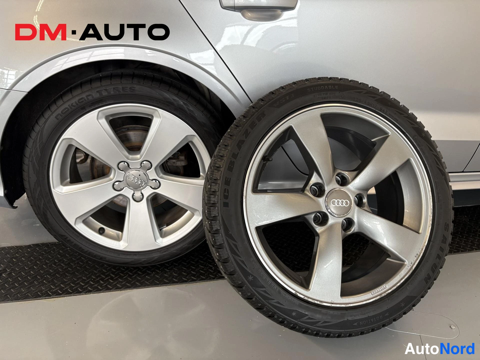 Muu: Auton kylki ja kaksi hopeaa viisipuomaista Audi-vannetta: toinen renkaalla autossa, toinen erikseen kuvassa.