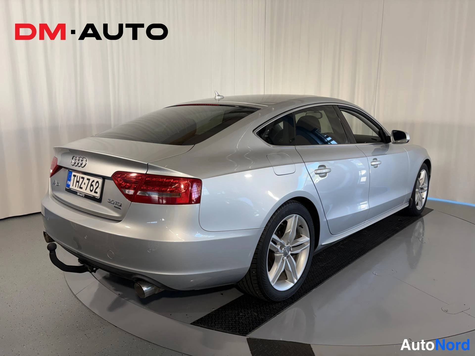 Takaviisto: Hopeinen Audi A5 Sportback takaa vinosti vasemmalta kuvattuna, rekisteritunnus, valuraudat ja kiintävä hinauskoulu näkyvät.