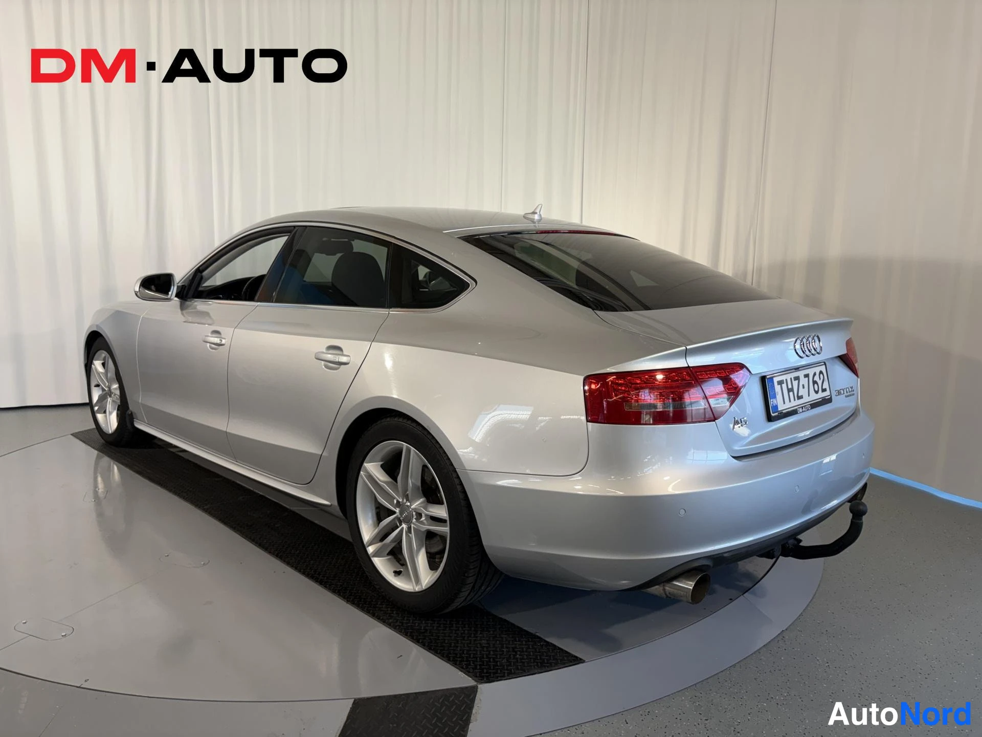 Takaviisto: Hopeinen Audi A5 Sportback takaa vinosti oikealta kuvattuna, rekisteritunnus ja hinauskoulu näkyvät.