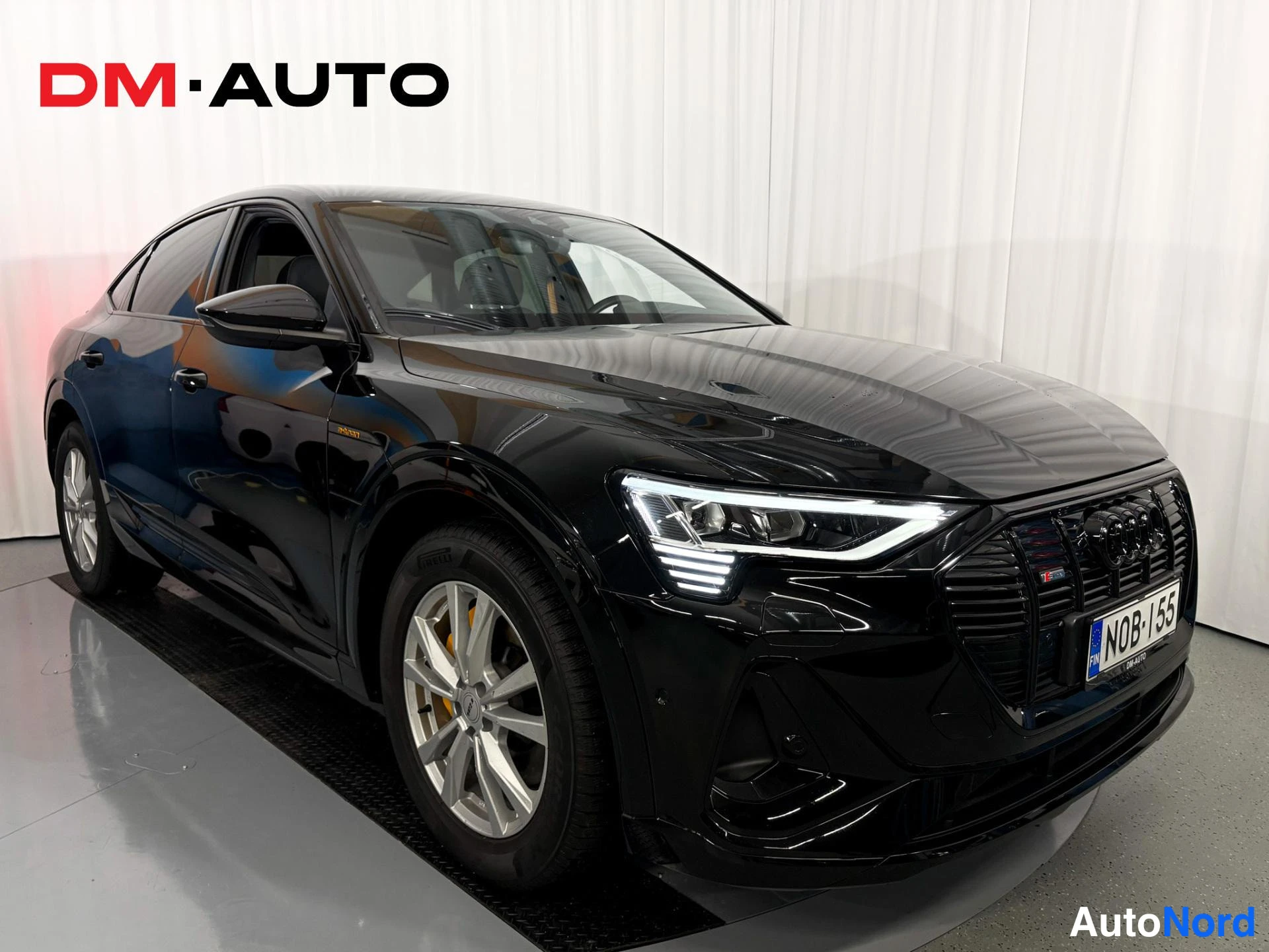 Etuviisto, nokka oikealle: Mustan Audi Sportbackin etukulmanäyttö oikealta: etusäleikkö ja LED-ajovalot oikealla, kylki hopeavanteilla ja oranssit jarrusatulat.