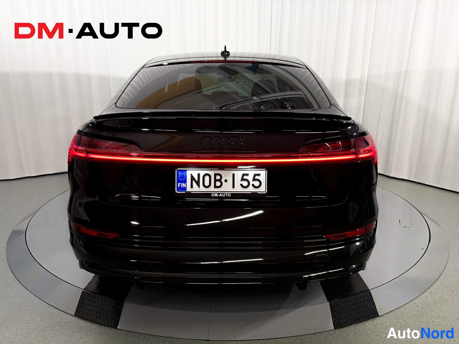 Takaa: Mustan Audi e-tron Sportbackin takaosa suoraan takaa; kirkkaat punaiset takavalot, Audi-merkki ja rekisterikilpi.