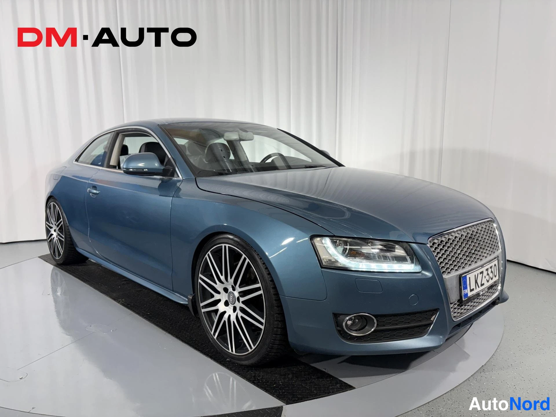 Etuviisto, nokka oikealle: Sinisenharmaa Audi A5 -coupé etukulmasta oikealta, rekisterikilpi ja monihaaraiset kevytmetallivanteet näkyvissä.