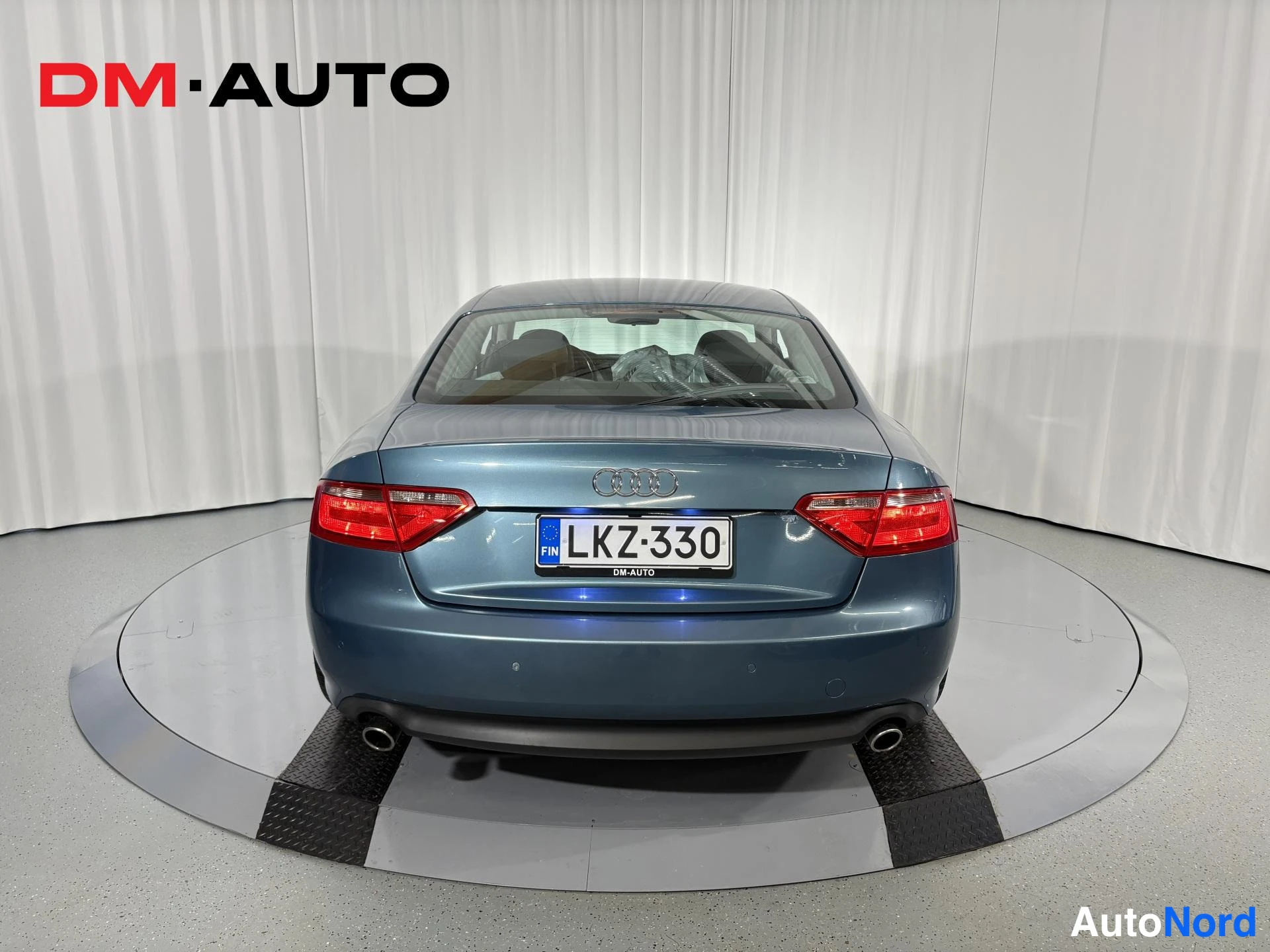 Takaa: Sininen Audi A5 -coupe suoraan takaa kuvattuna, näkyvissä neljä pyöreää kromihynttiä, takavalot ja rekisterikilpi.