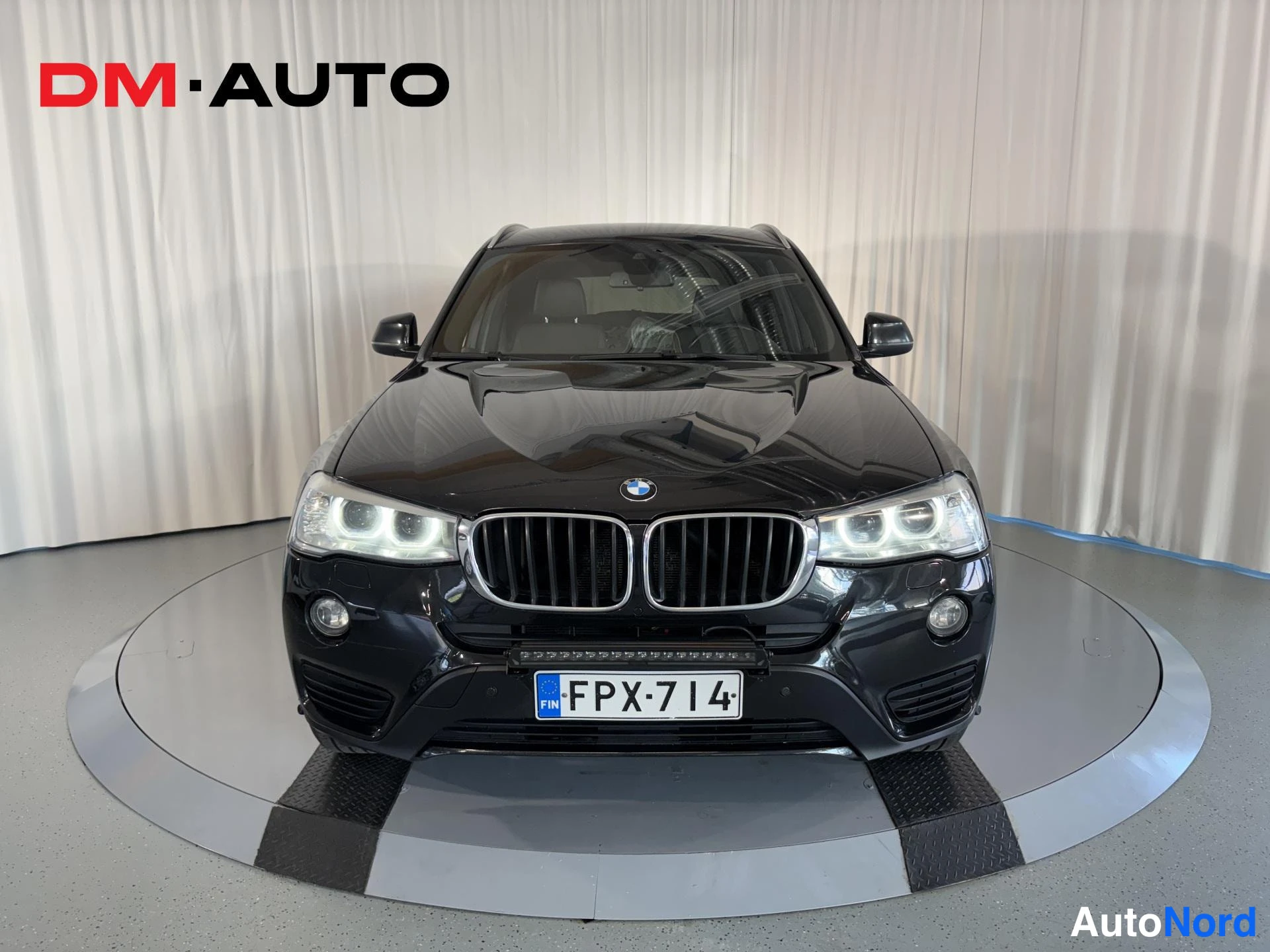 Edestä: Musta BMW X3 suoraan edestä, etusäleikön ja ajovalojen ympärillä valokuvausliikkeen studio-asetelma.