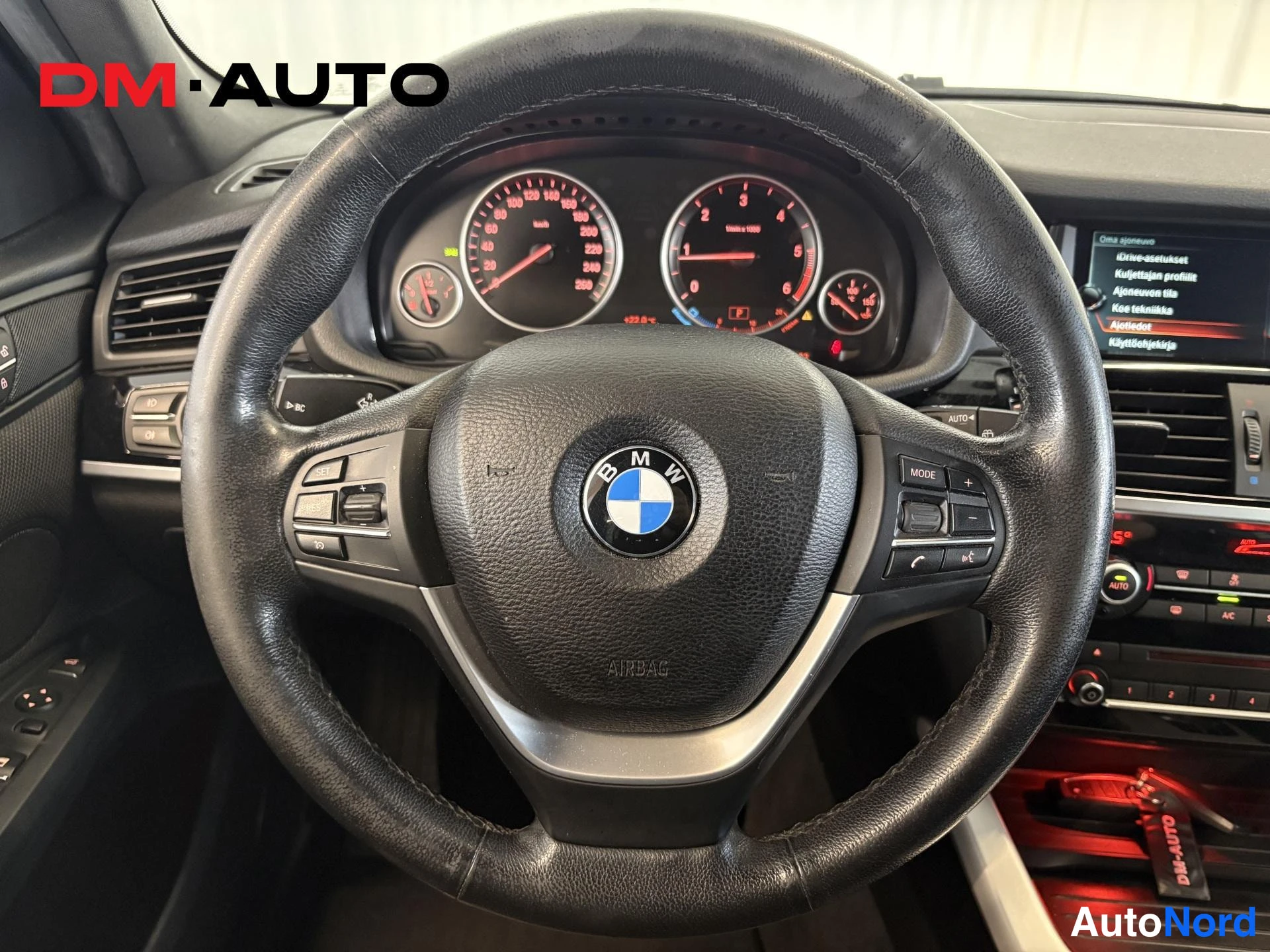 Muu: Lähikuva ohjauspyörästä BMW-logolla, taustalla mittaristo ja osa kojelautaa sekä näytöstä.