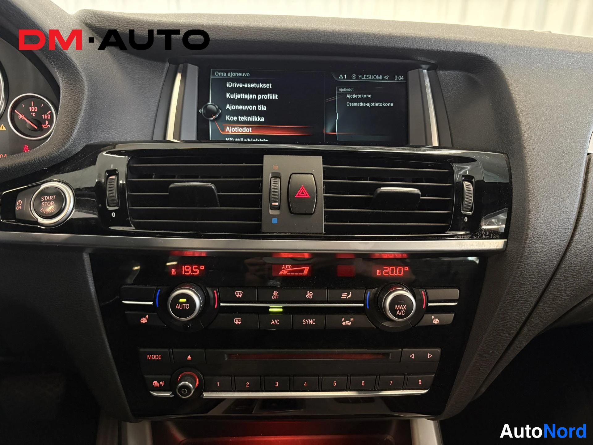 Yksityiskohta: Keski:konsoli: infotainment-näyttö Oma ajoneuvo -valikolla, ilmastointipaneeli näyttää 19,5° ja 20,0°, AUTO- ja MAX A/C-painikkeet, START STOP -painike ja 1-8 n