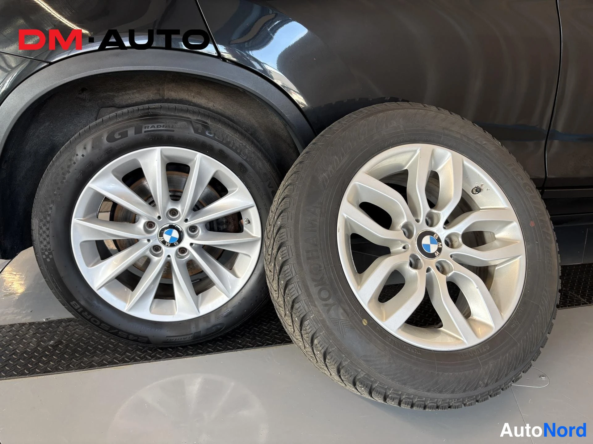 Yksityiskohta: Musta auto etupyörällä GT Radial -renkaalla ja vieressä irrotettu talvirengas Nokian valumiisillä vanteella.