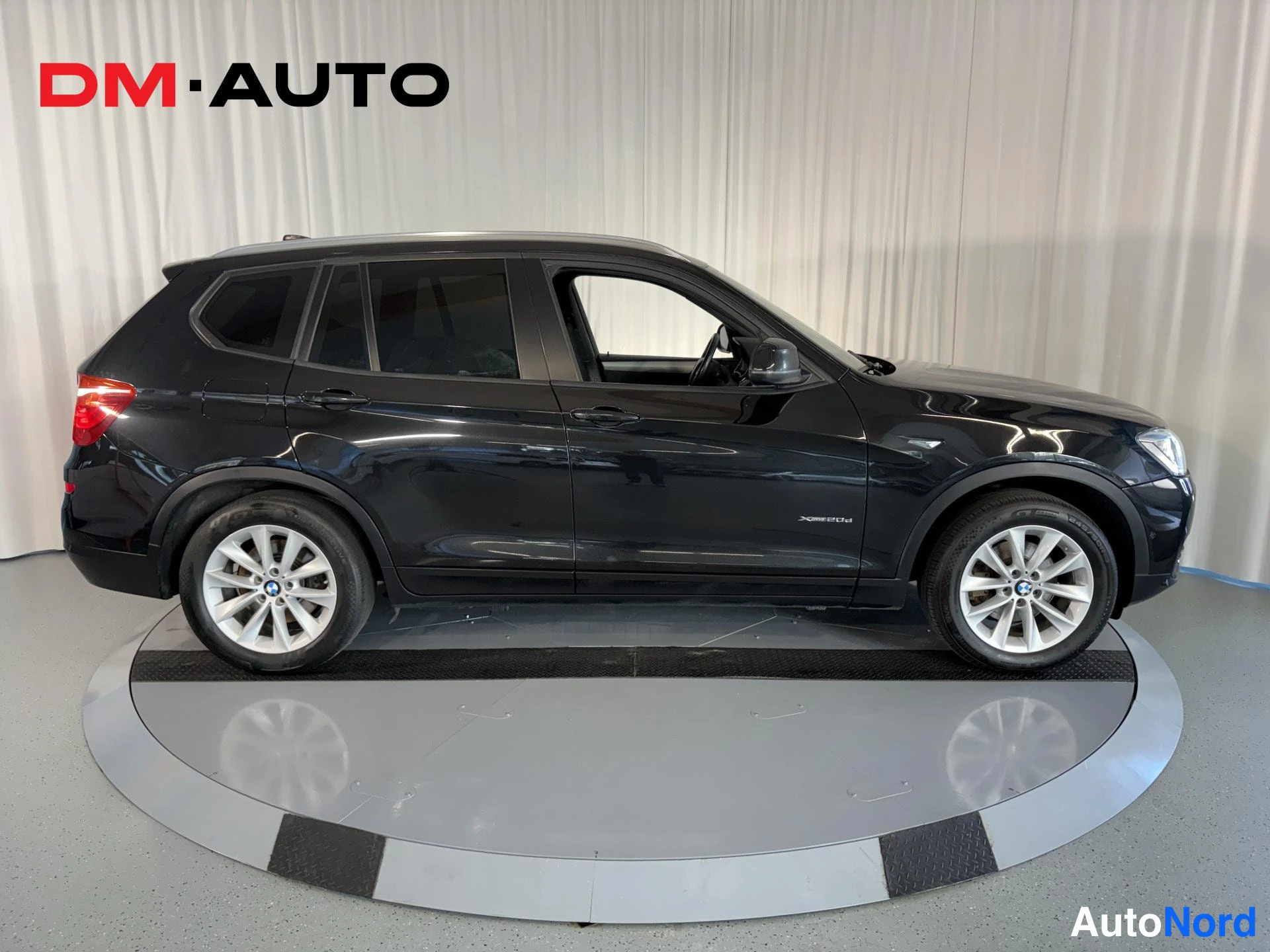 Sivulta: Musta BMW X3 sivuprofiilista, kuljettajan puoleinen kylki näkyy, valokuvausliikkeen pyörivällä alustalla.
