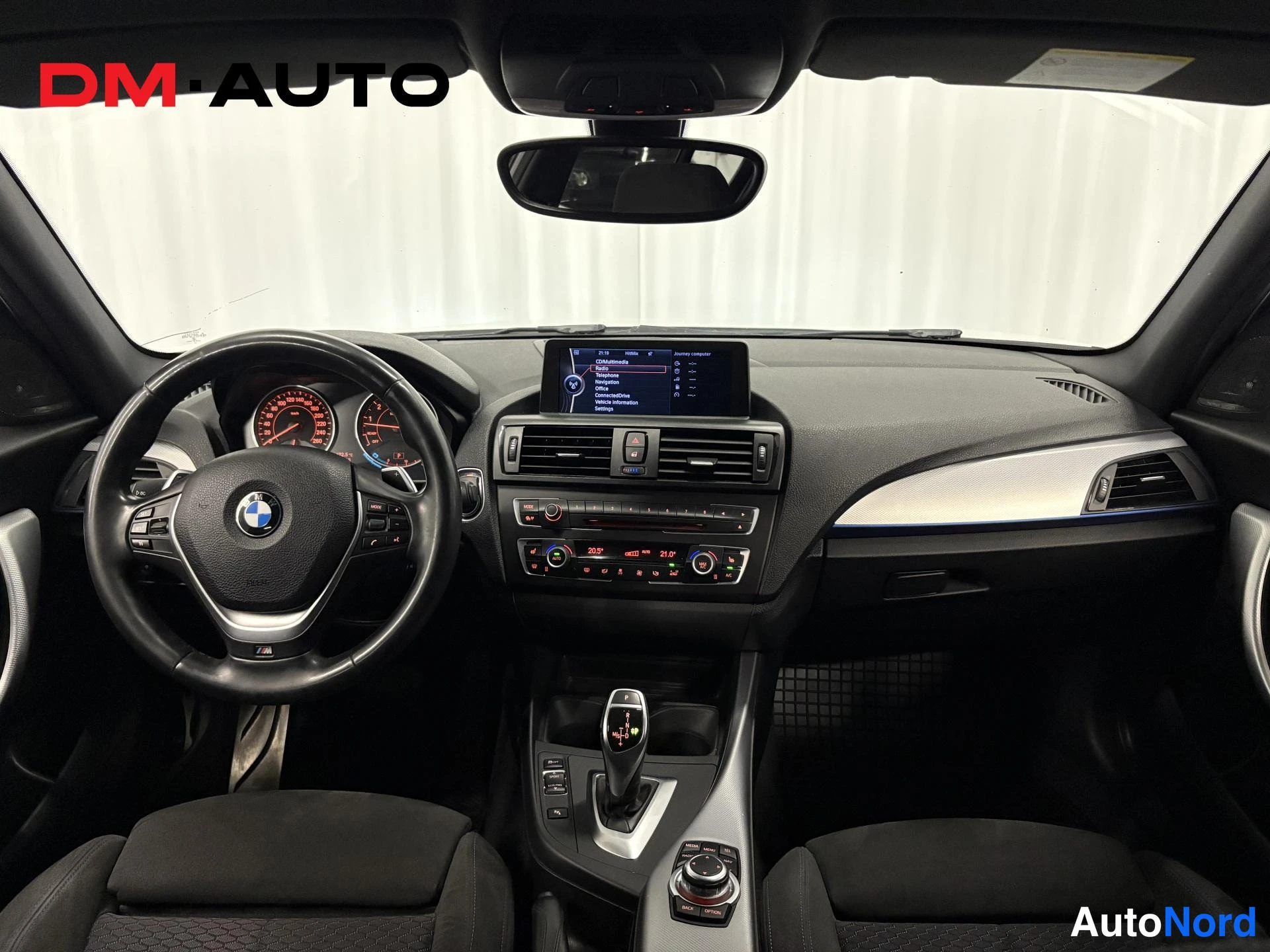 Etuviisto, nokka vasemmalle: Näkemys kojelautaan keskikonsolosta: BMW-ohjauspyörä, peräkkäisvaihteistotunneli, automaattivalitsin, iDrive-ohjain ja ylhäällä irrotettava näyttö, jos