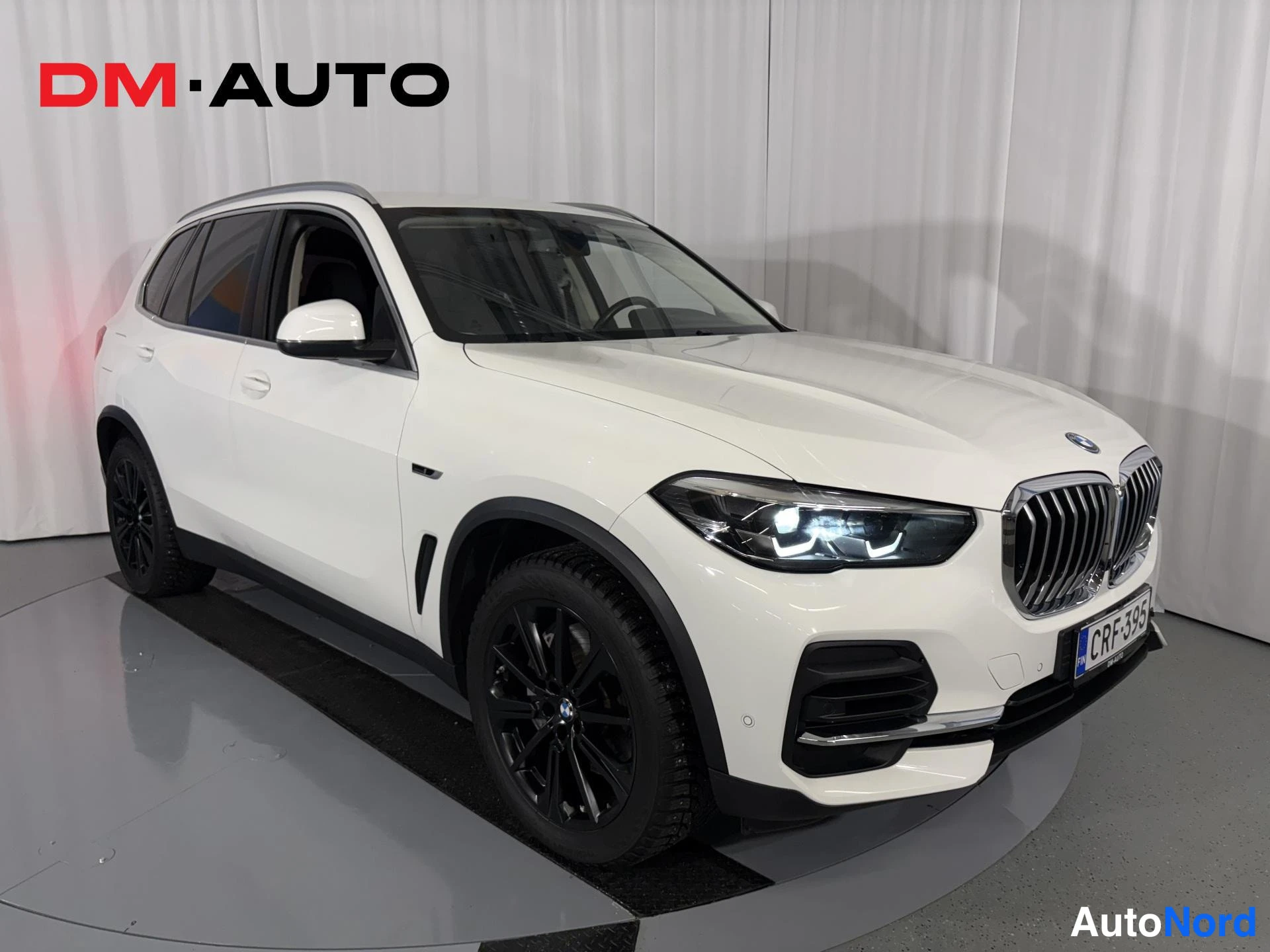 Etuviisto, nokka oikealle: BMW X5, valkoinen, etuosa oikealta kolmasosan kuvakulmasta; mustat pyöränkotelot ja tummat vanteet näkyvät.