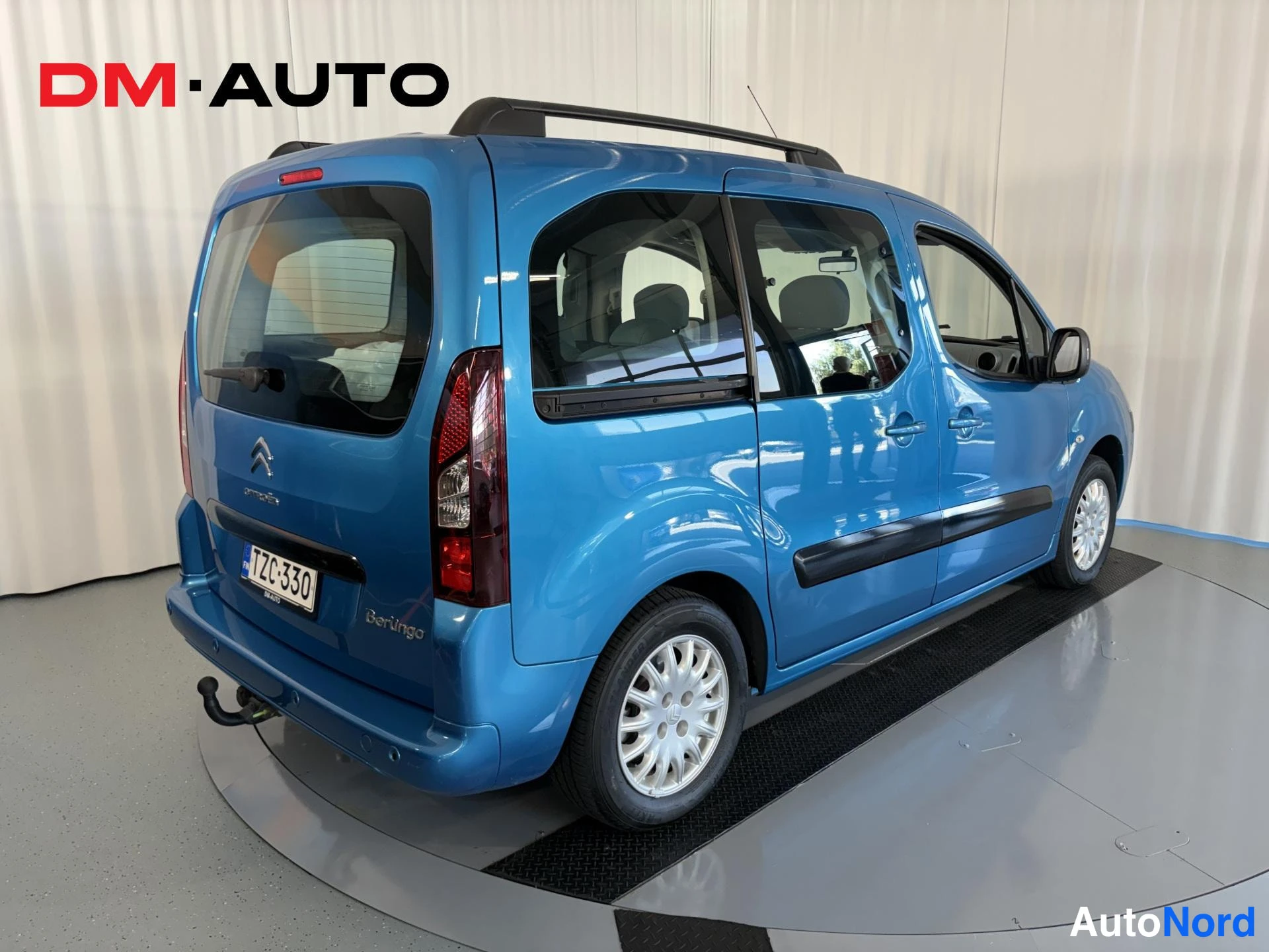 Takaviisto: Sininen Citroën Berlingo takaa sivulta, kattokaiteet ja vetokoukku näkyvissä, rekisteritunnus.