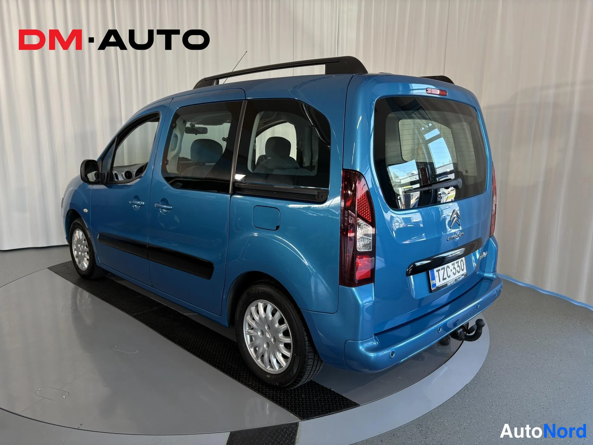 Takaviisto: Sininen Citroën Berlingo takaa sivulta vasemmasta kulmasta, kattokaiteet ja vetokoukku näkyvissä, rekisteritunnus.