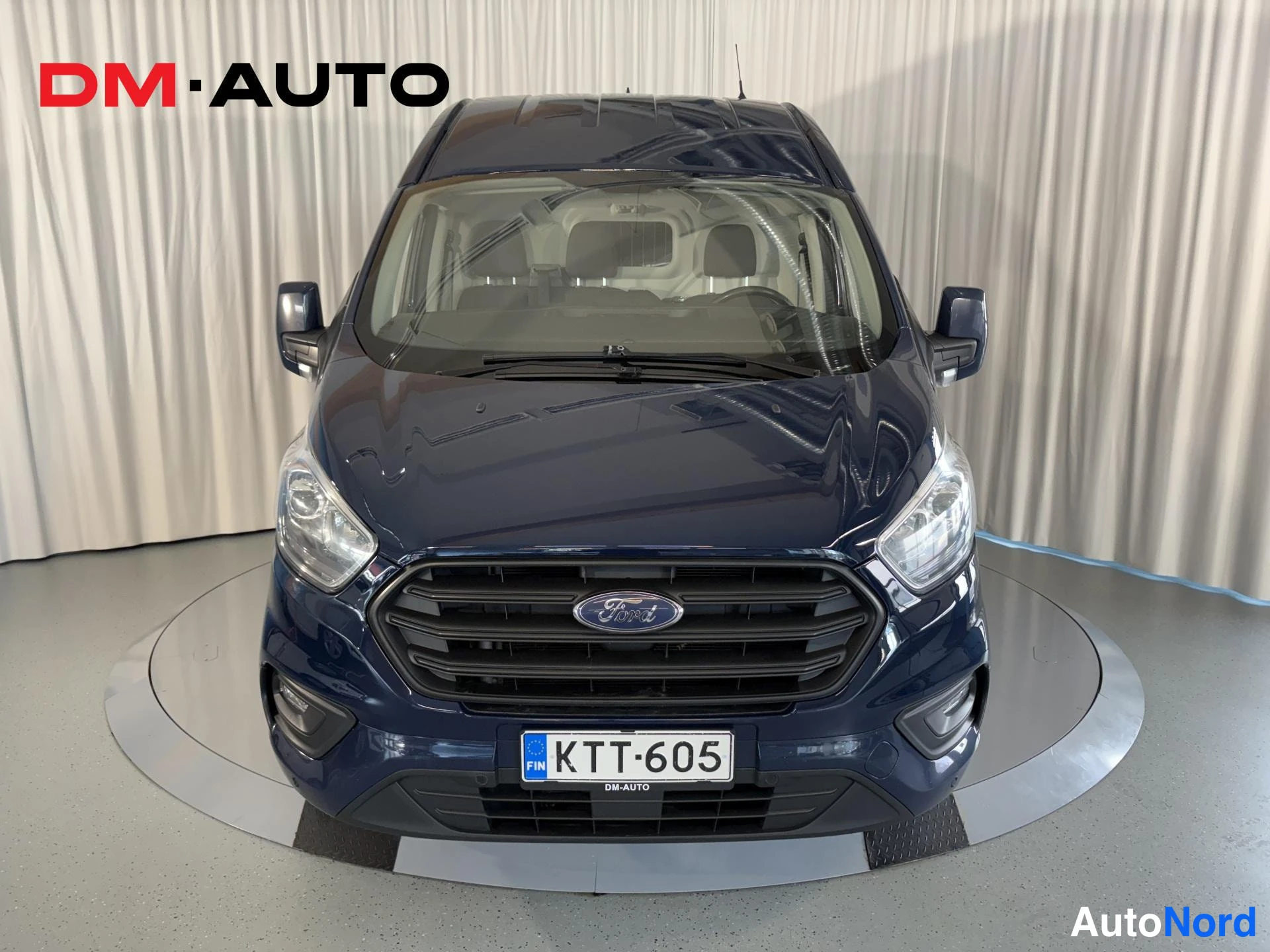 Edestä: Sininen pakettiauto suoraan edestäpäin, Ford-merkki etusäleikössä ja rekisterikilpi näkyvissä.