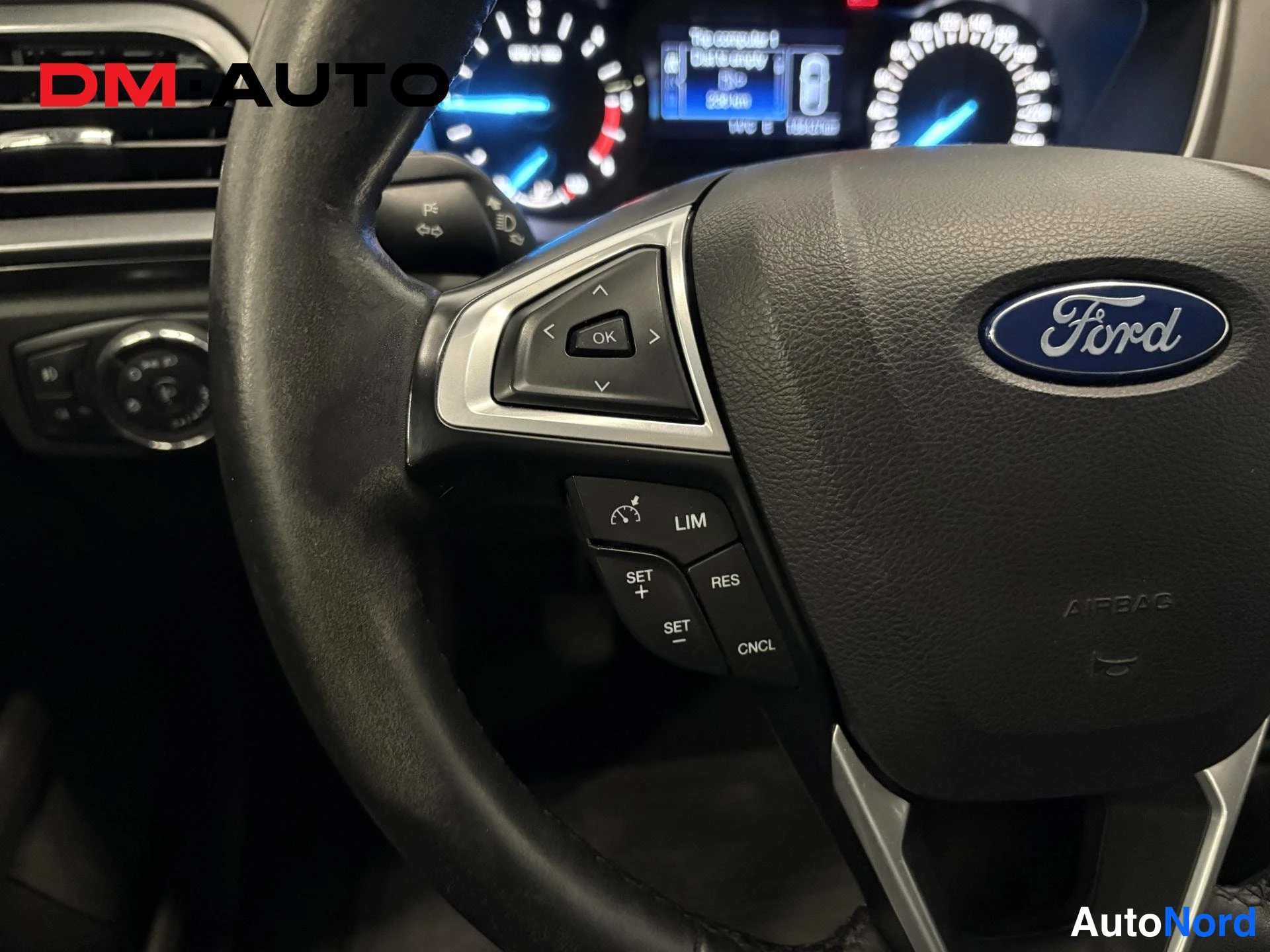 Muu: Vaihdinta- ja mittariston lähipäivitys Ford Mondeon ohjauspyörästä: Ford-tunnus, LIM-, SET-, RES- ja CNCL-napit sekä OK- ja nuolinäppäimet; taustalla mittaristo