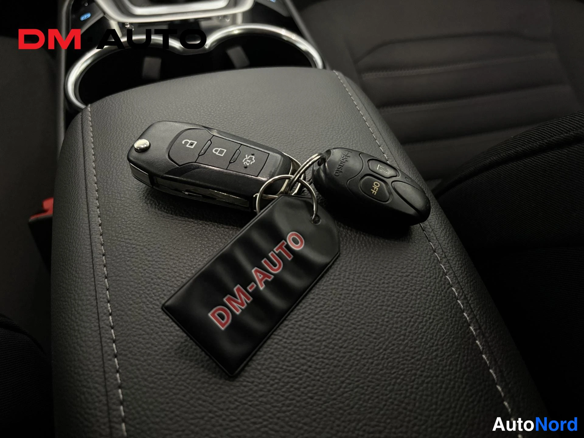 Sivulta: Kaksi avainkärynnettä ja musta DM-AUTO-avainlappu keskitunnelin käsinojalla.